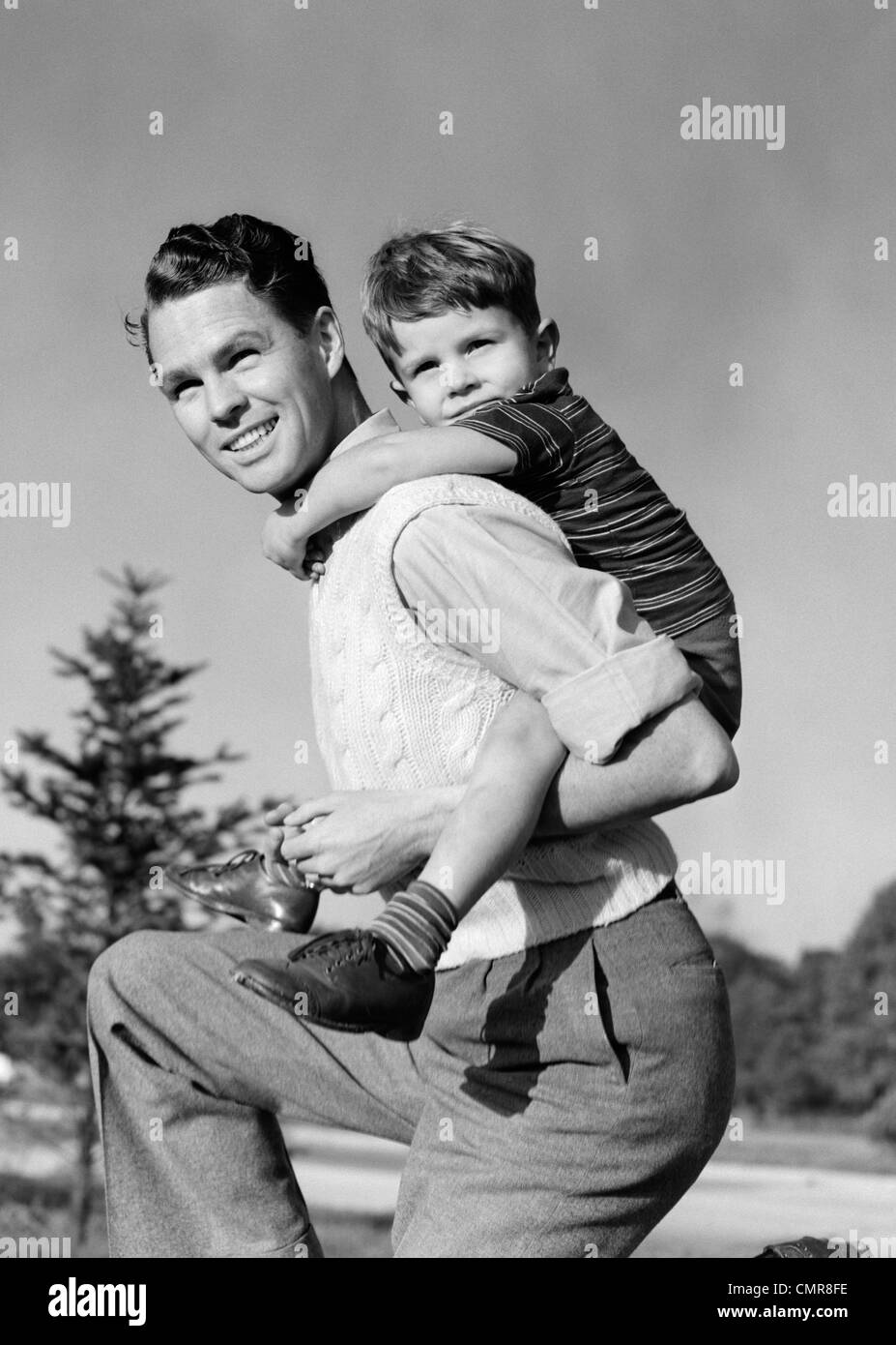 1940s SMILING FATHER CARRYING SON PIGGYBACK ON BACK Stock Photo