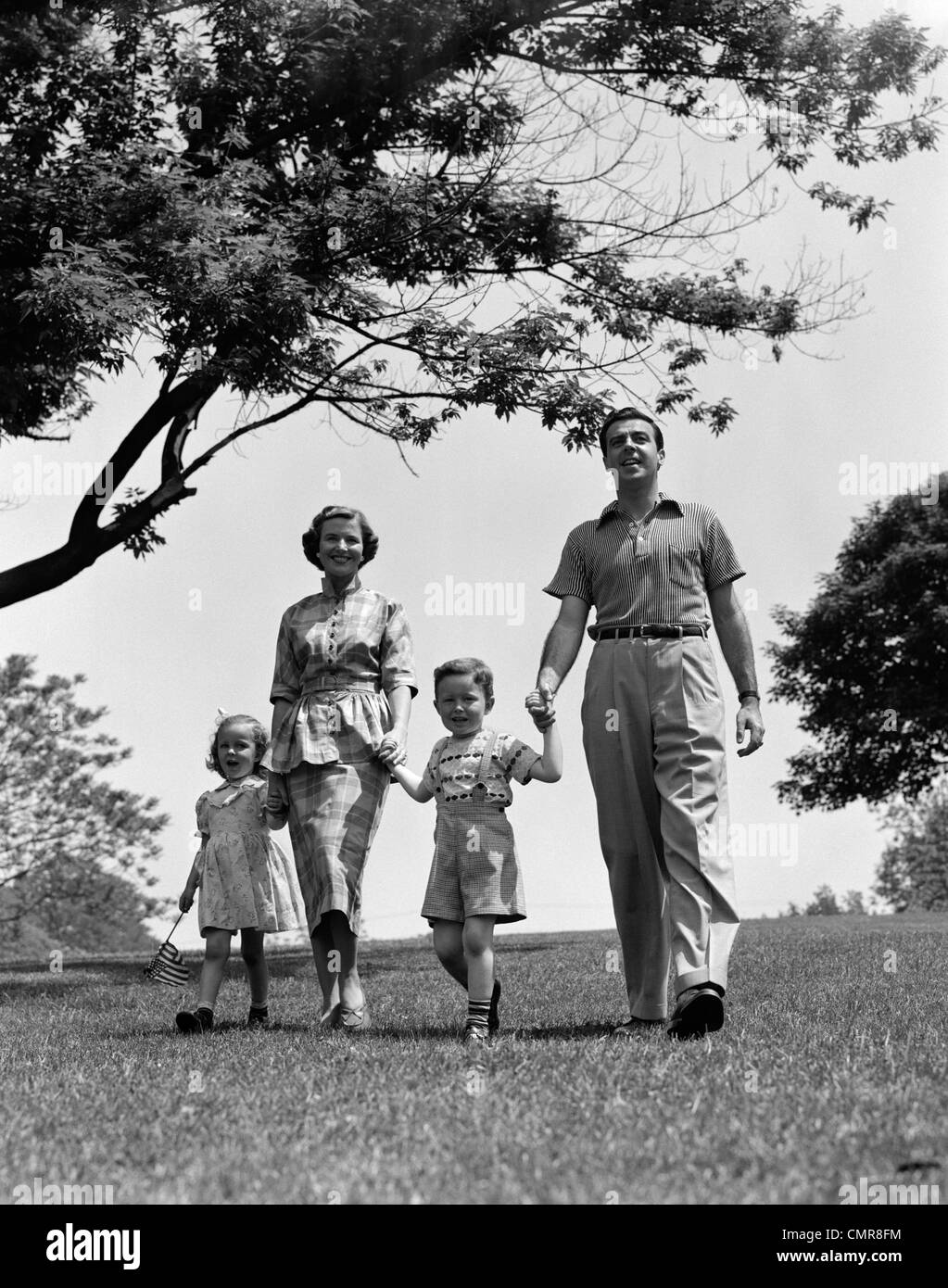 1950s HAPPY FAMILY MOTHER FATHER DAUGHTER SON WALKING IN PARK Stock Photo