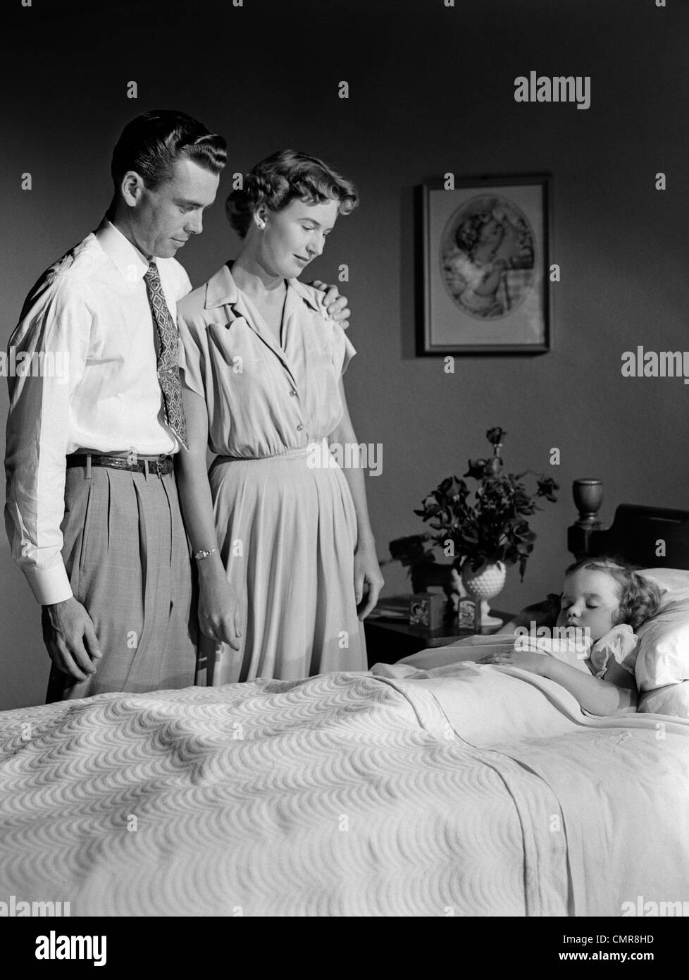1950s MOTHER AND FATHER WATCHING SLEEPING DAUGHTER Stock Photo