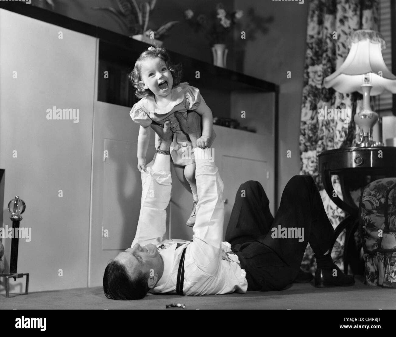 1950s FATHER LYING FLOOR HOLDING DAUGHTER GIRL UP IN THE AIR Stock Photo