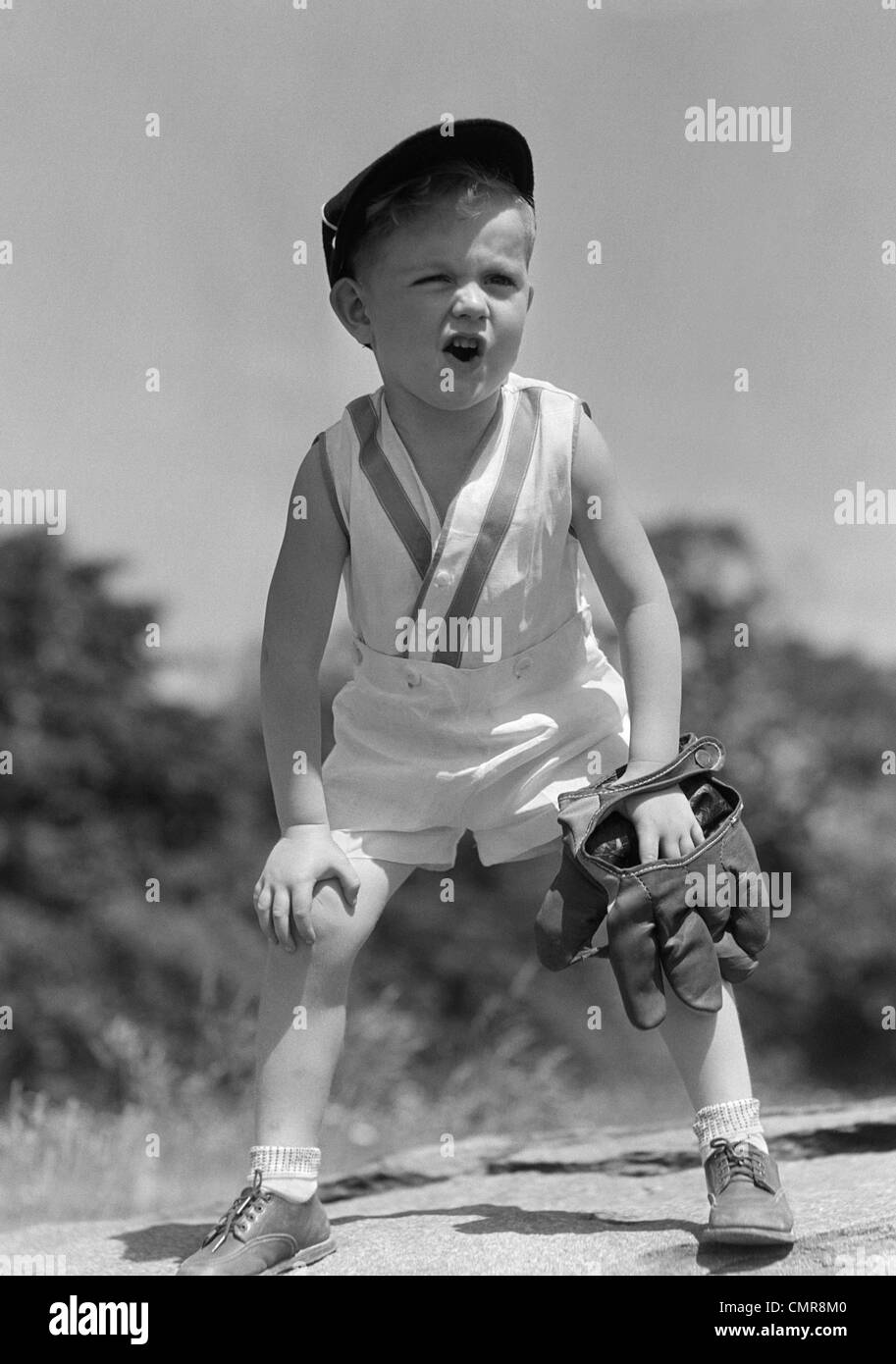 1930s BOY WEARING BASEBALL HAT & GLOVE BENT OVER WITH HANDS ON KNEES YELLING Stock Photo