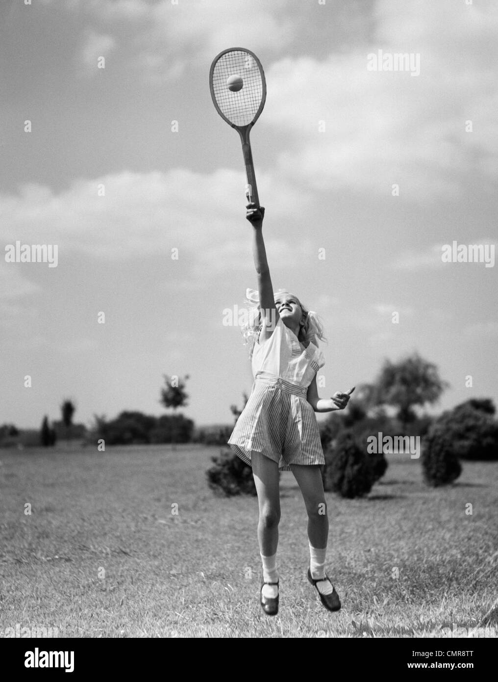 1930s GIRL PLAYING TENNIS JUMPING TO HIT BALL OVERHEAD Stock Photo
