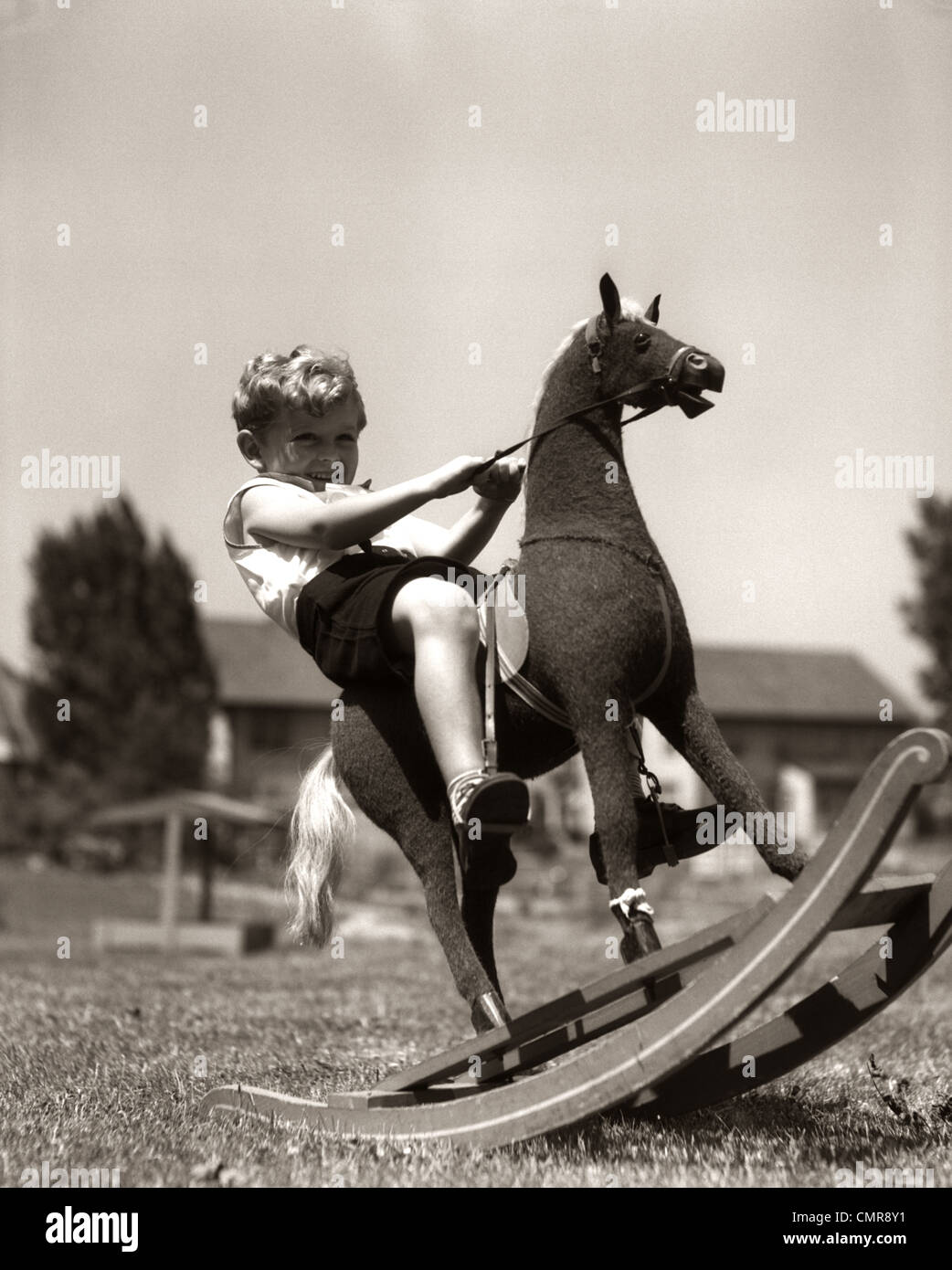 1930s LITTLE BOY OUTSIDE PLAYING RIDING ON TOY ROCKING HORSE Stock Photo