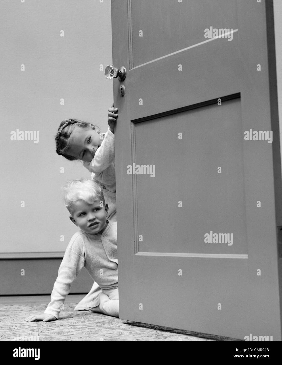 1940s CHILDREN BOY AND GIRL IN PAJAMAS PEEKING AROUND DOOR Stock Photo