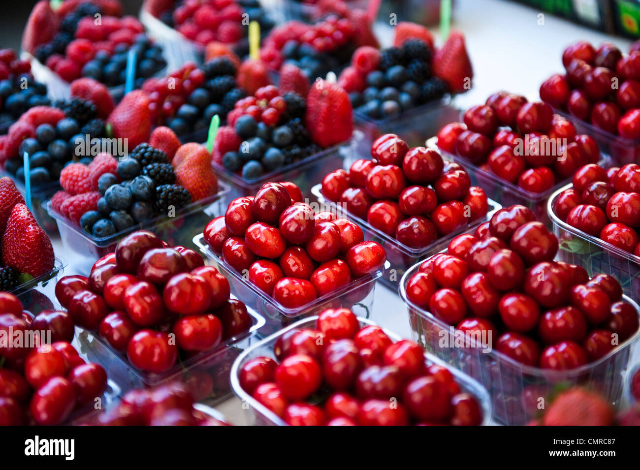 Cherries grouped together in mini clear containers; containers of mixed berries surround the containers of cherries. Stock Photo