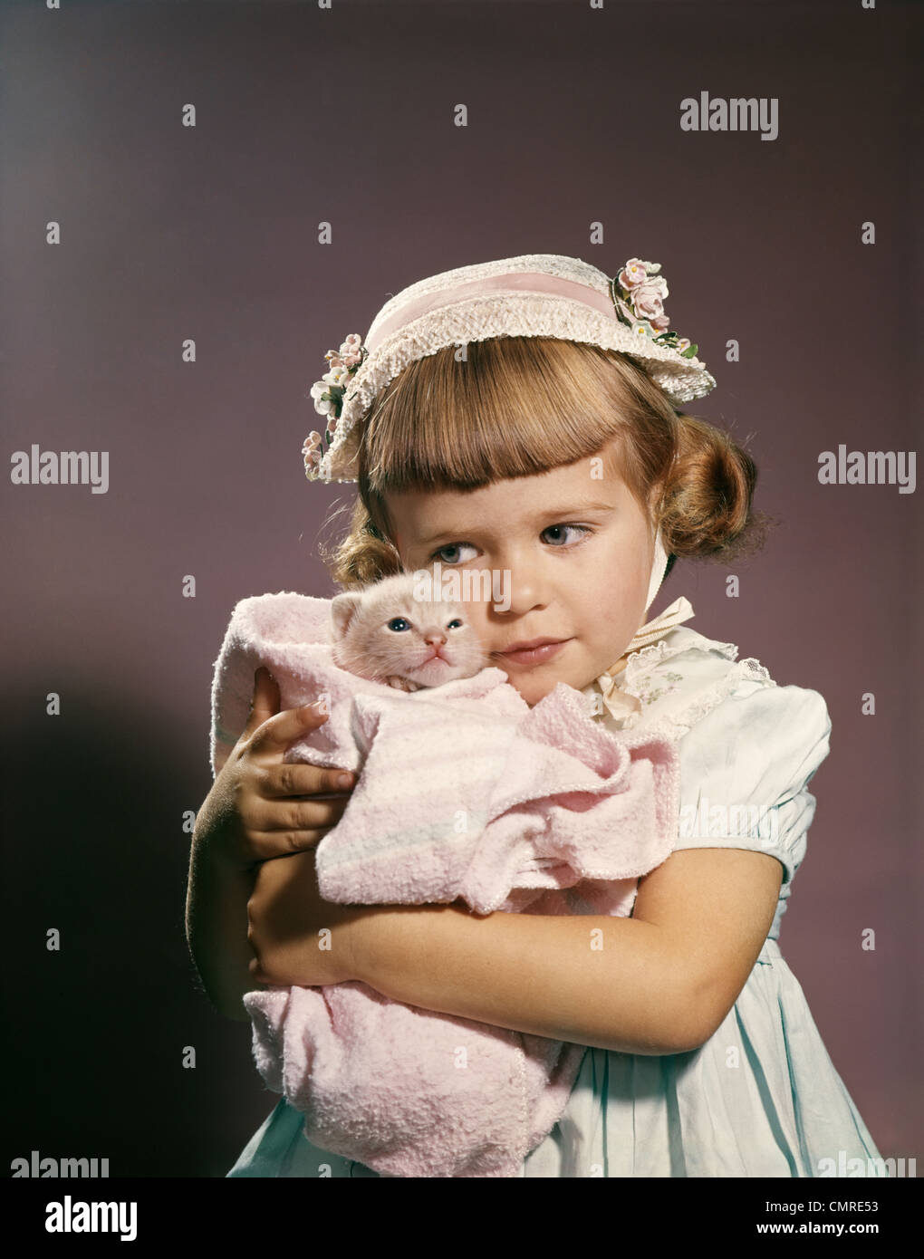1950s 1960s LITTLE GIRL IN EASTER HAT HUGGING A KITTEN Stock Photo