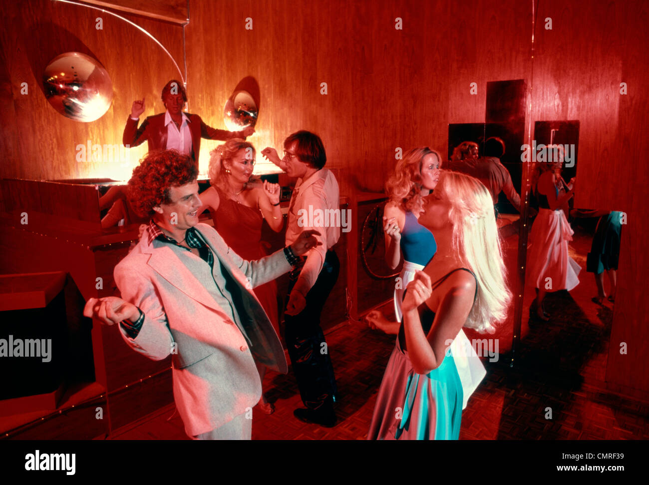1970s 1980s COUPLES MEN WOMEN DANCING DISCO DISCOTHEQUE INDOOR DJ IN BACK Stock Photo
