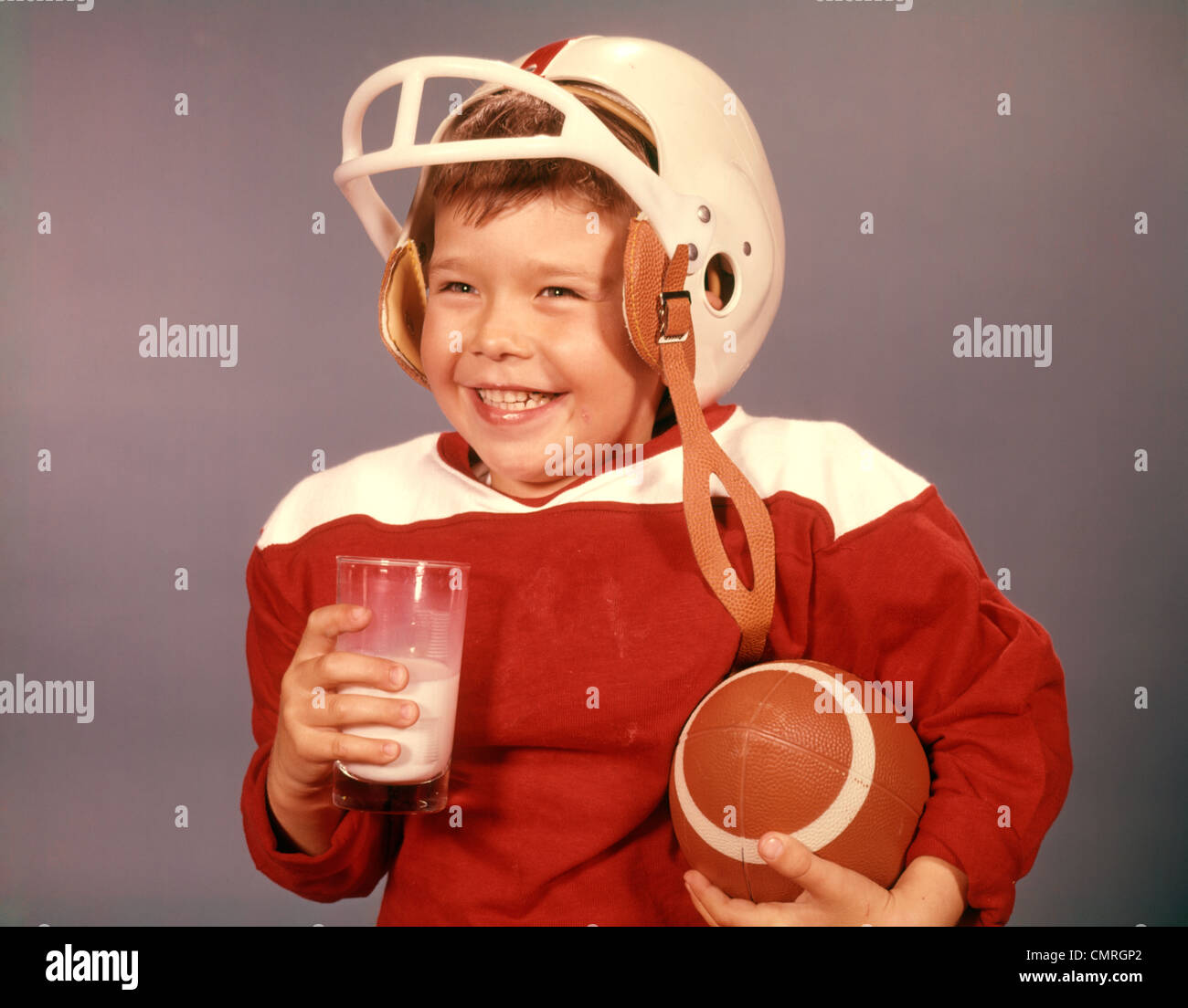 1960s BOY DRINKING MILK WEARING FOOTBALL HELMET RED JERSEY HOLDING BALL