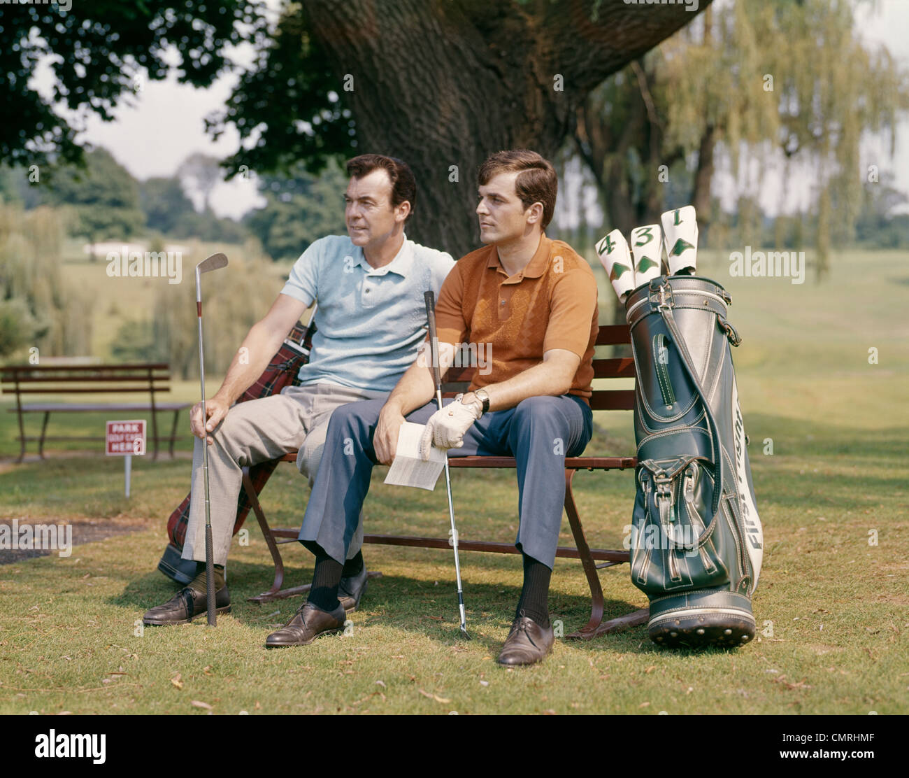 1960s TWO MEN SITTING UNDER TREE WAITING TO TEE-OFF Stock Photo