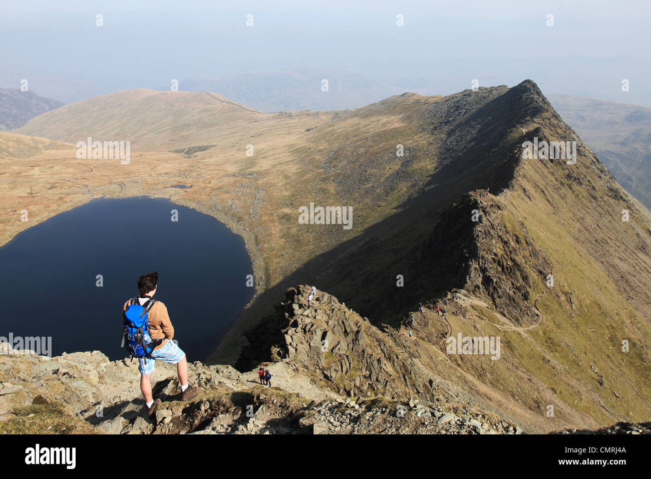 A young man looks down along Striding Edge with Red Tarn to the left, Helvellyn, Cumbria NW England UK Stock Photo