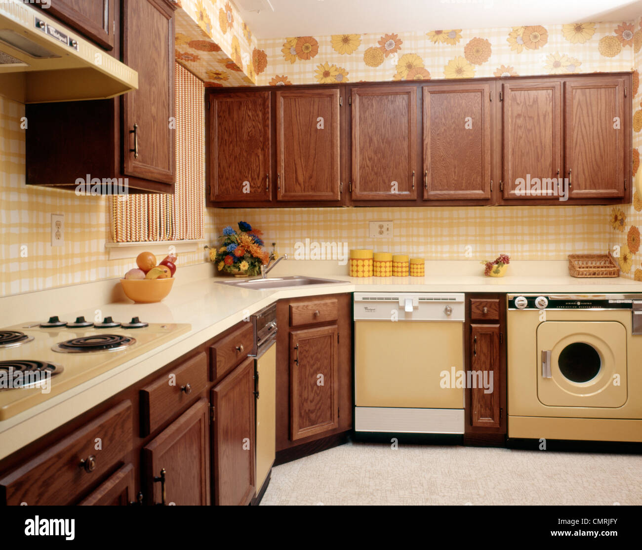 1970s KITCHEN INTERIOR WITH YELLOW APPLIANCES WOOD CABINETS AND SUNFLOWER FLORAL PRINT WALLPAPER Stock Photo