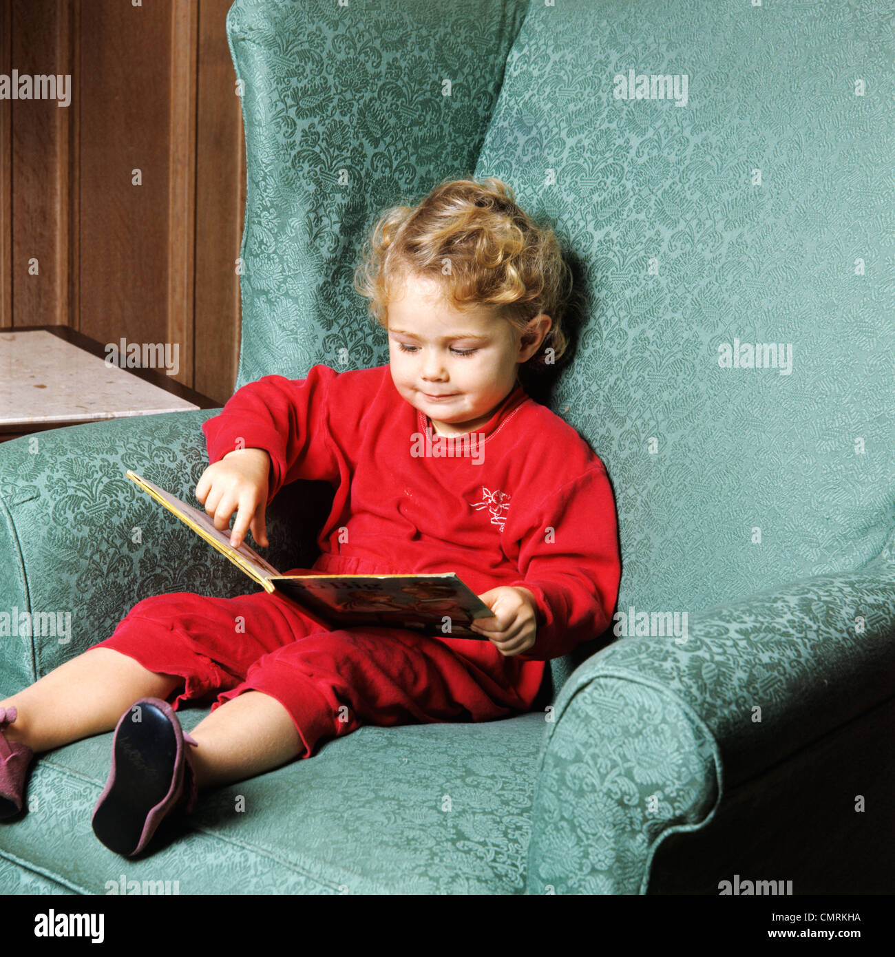 1970s TODDLER GIRL SITTING IN CHAIR READING BOOK RETRO Stock Photo