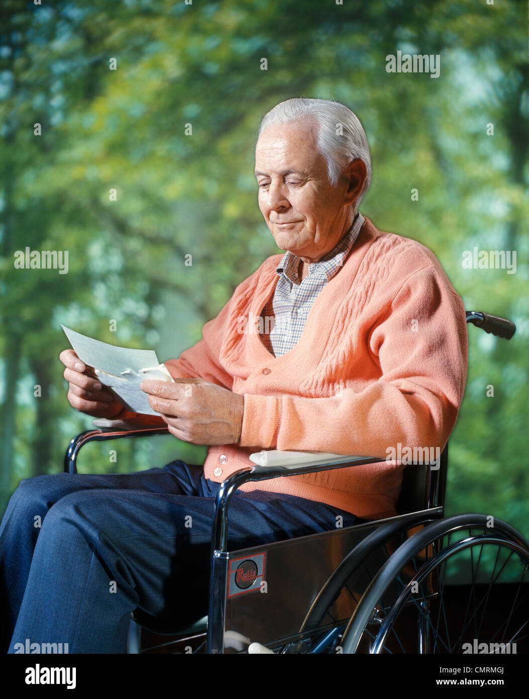 1970 1970s RETRO COMPOSITE IMAGE SMILING SENIOR ELDERLY MAN SITTING IN WHEELCHAIR READING LETTER IN WOODS NATURE OUTDOORS Stock Photo