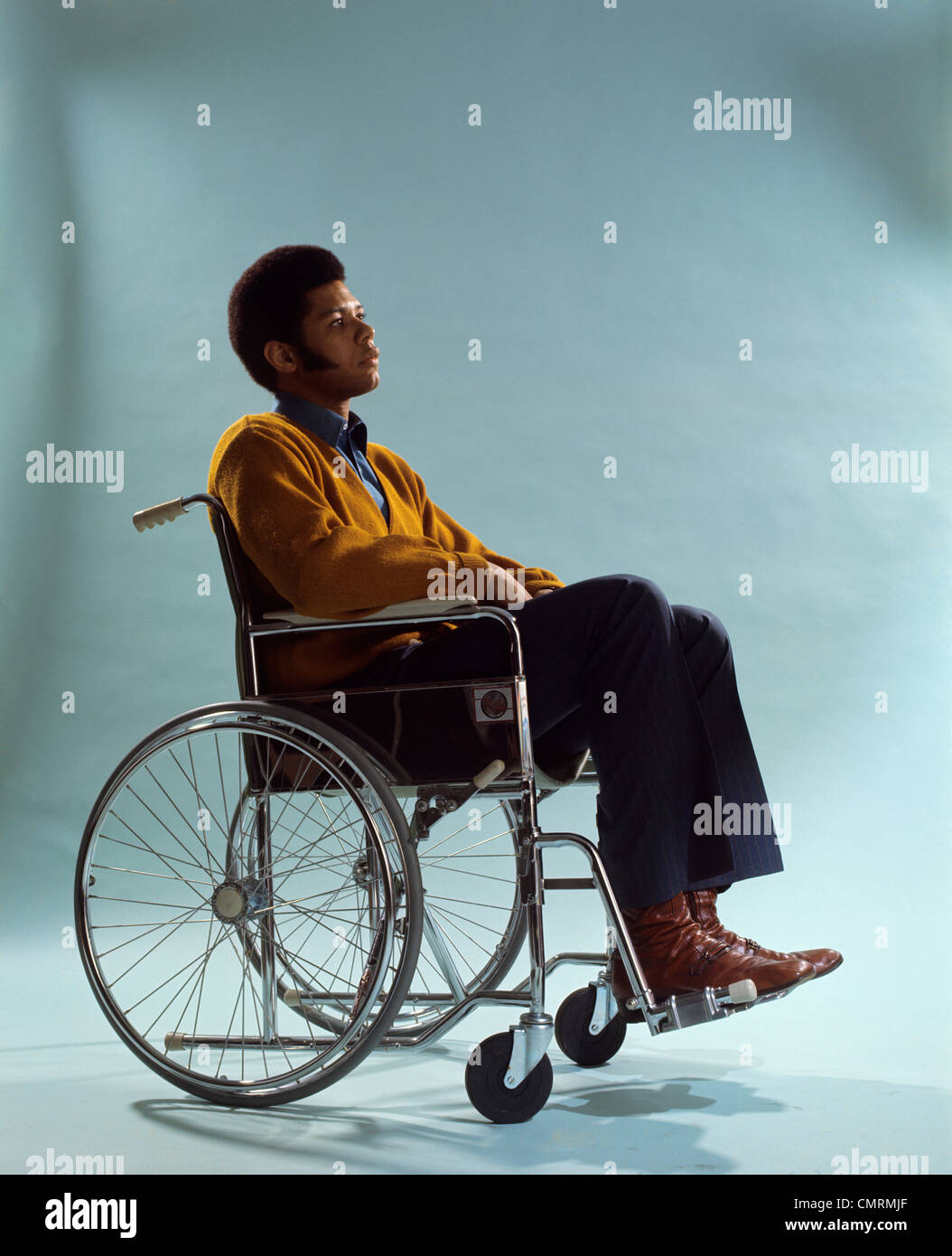 1970s AFRICAN-AMERICAN MAN SITTING WHEELCHAIR RETRO Stock Photo
