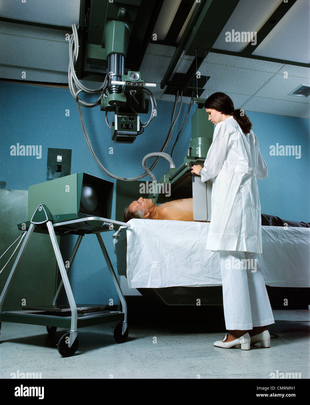 1970s FEMALE X-RAY TECHNICIAN WORKING WITH SENIOR MALE PATIENT MAN WOMAN RETRO Stock Photo