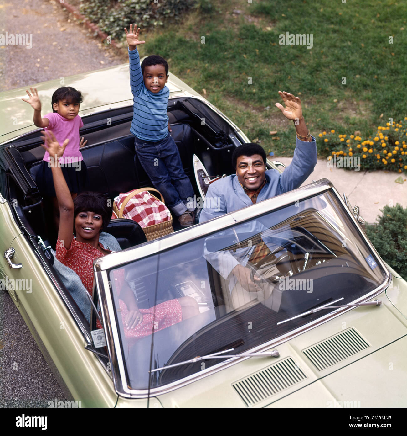 AFRICAN-AMERICAN FAMILY FATHER MOTHER SON DAUGHTER WAVING FROM CONVERTIBLE CAR OUTDOOR 1970s Stock Photo