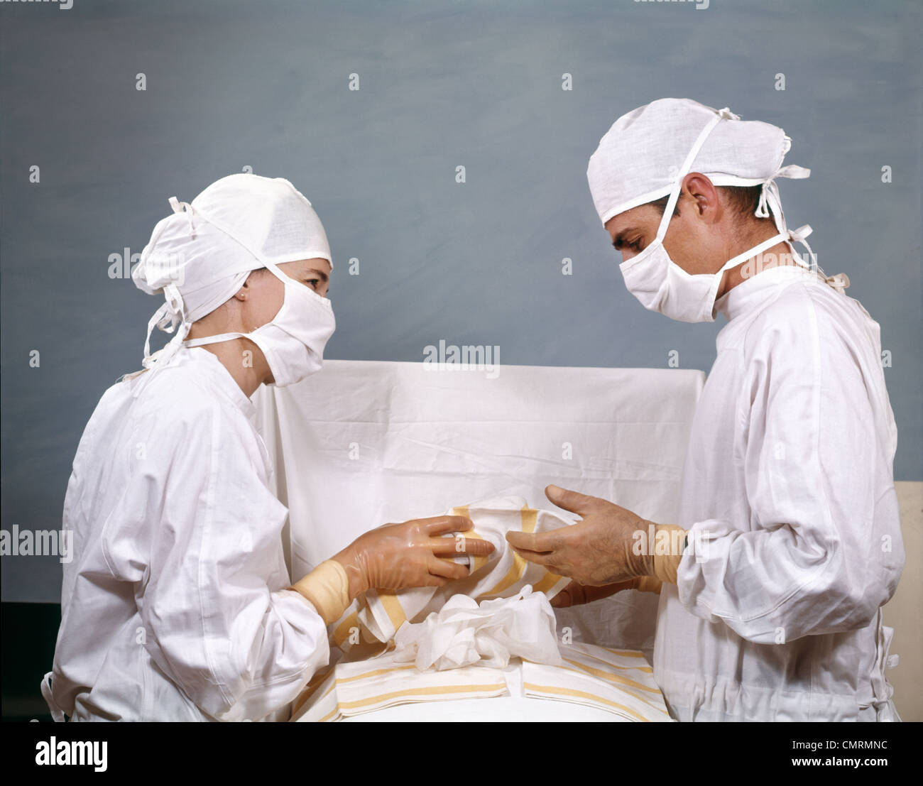 1950s 1960s DOCTOR & NURSE IN SURGERY OPERATION OPERATING STERILE SURGICAL WHITE CAPS GOWNS MASKS RETRO VINTAGE Stock Photo