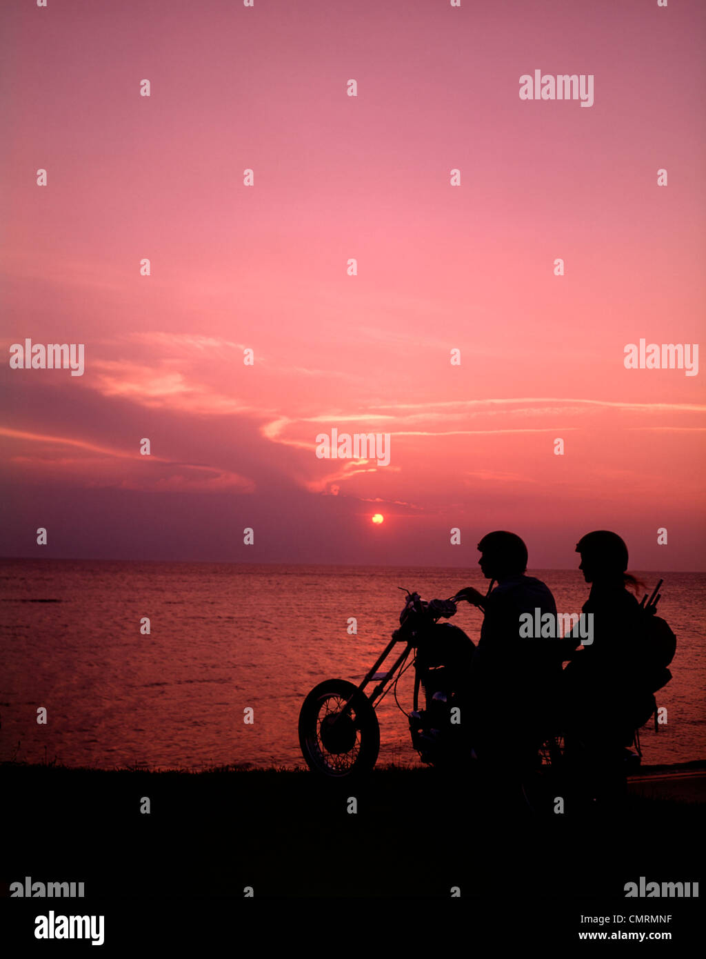 1970 1970s SILHOUETTED COUPLE SUNSET BEACH RIDING CHOPPER MOTORCYCLE BIKE MOTOR CYCLE MOTORCYCLES BIKERS BIKES Stock Photo