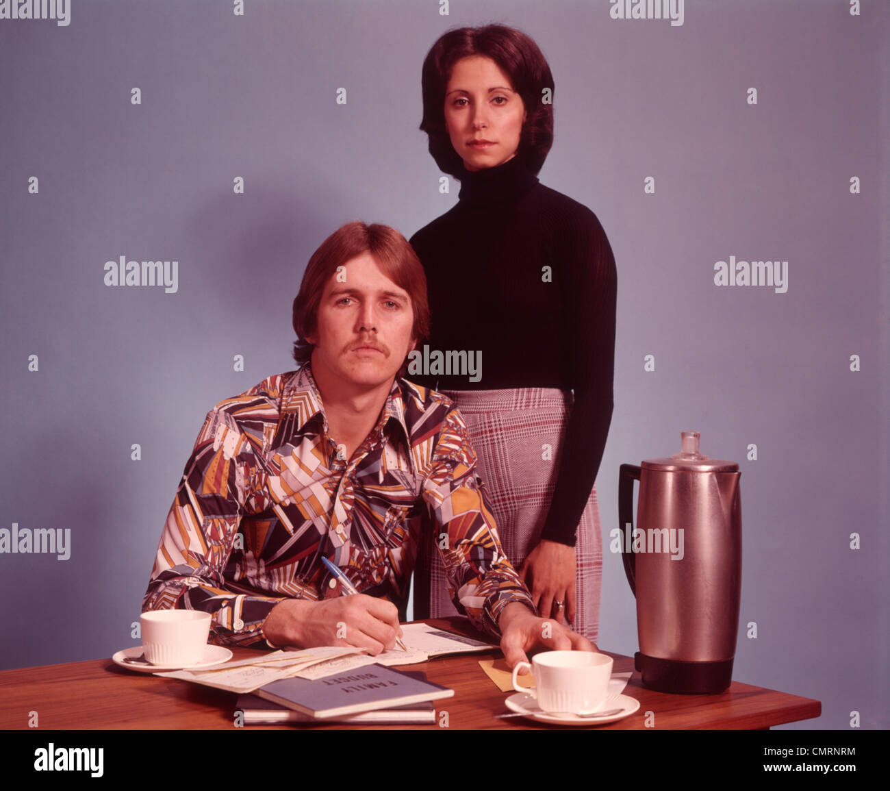 1970 1970s COUPLE HUSBAND WEAR PRINT SHIRT WIFE STANDS BEHIND GO OVER BUDGET HOUSEHOLD FINANCE COFFEE POT RETRO RRR Stock Photo