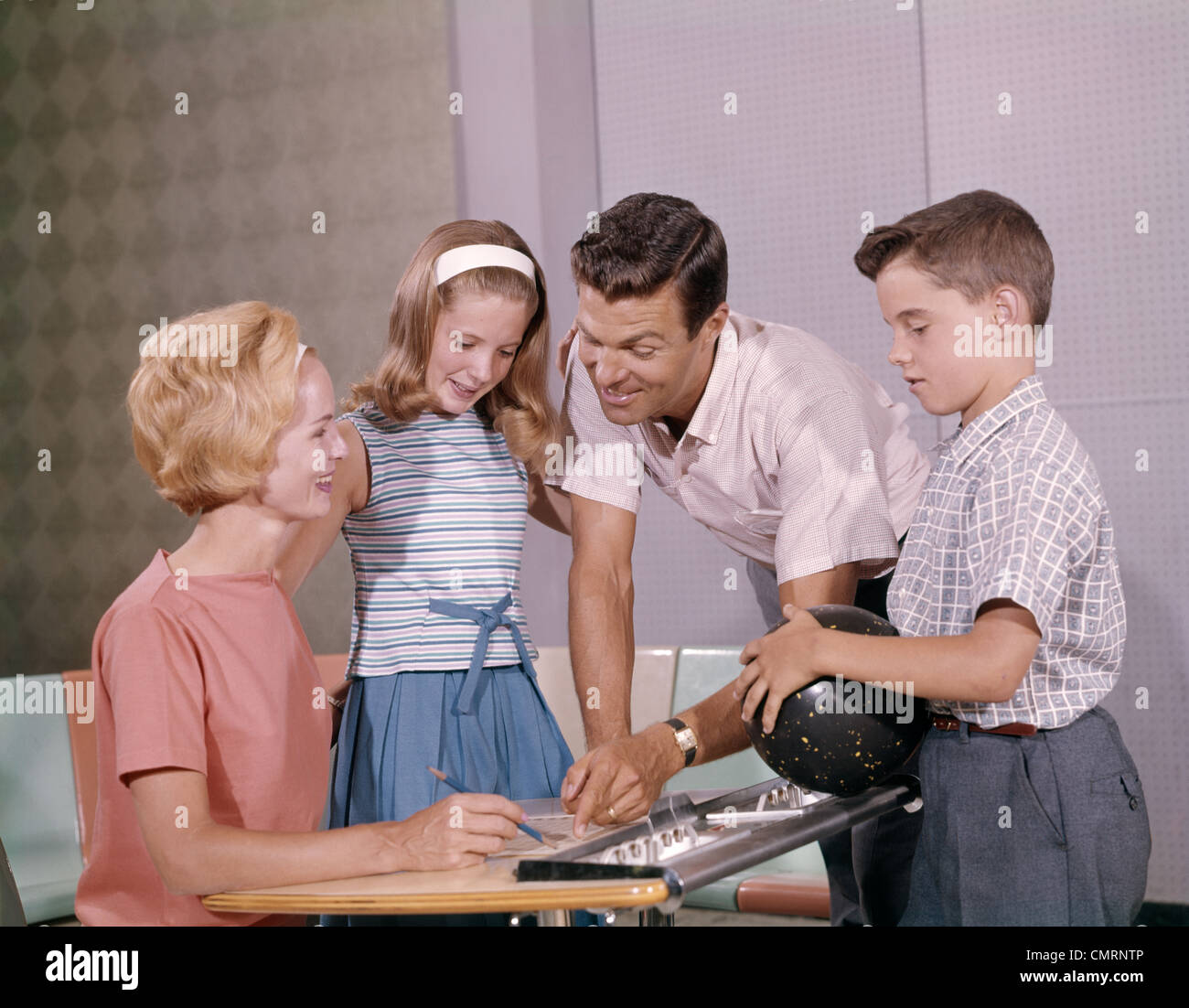 FAMILY MOTHER FATHER DAUGHTER SON TOGETHER BOWLING LOOKING AT SCORE INDOOR 1960s Stock Photo
