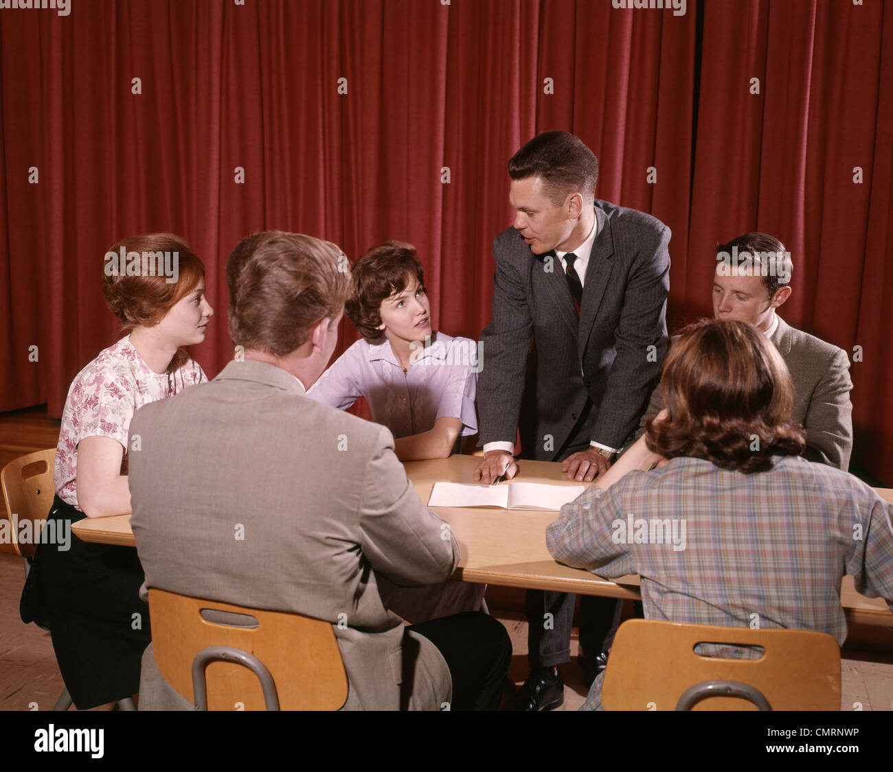 1960s GROUP OF SIX STUDENTS SITTING AT AROUND A TABLE TALKING THREE BOYS THREE GIRLS TEENAGE INDOOR Stock Photo
