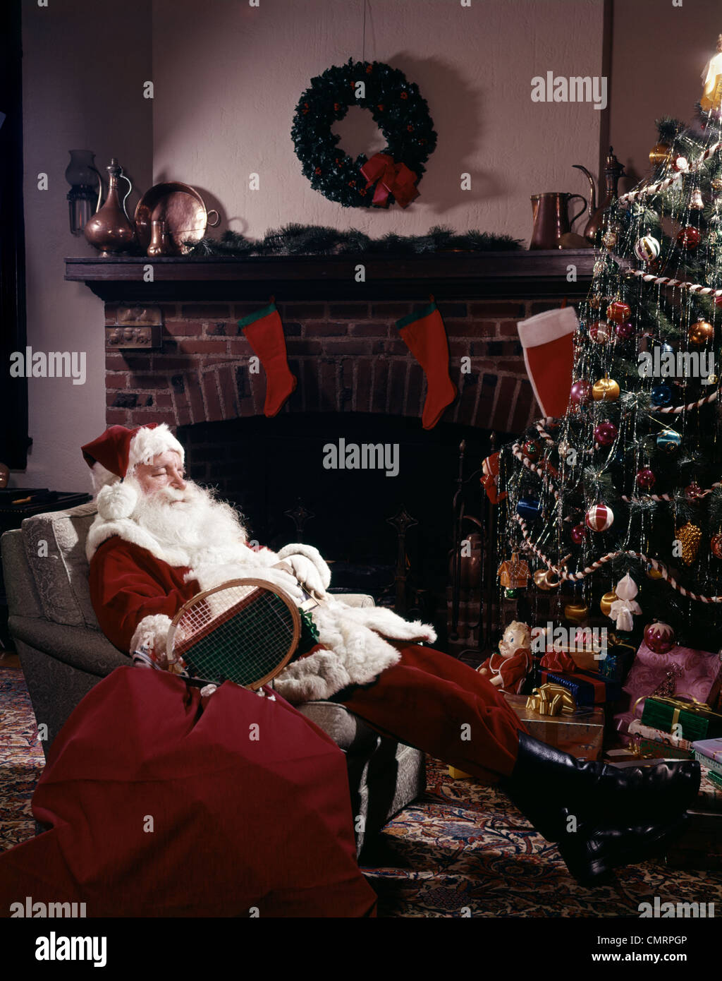 SANTA CLAUS ASLEEP IN CHAIR IN FRONT OF CHRISTMAS TREE AND FIREPLACE INDOOR Stock Photo