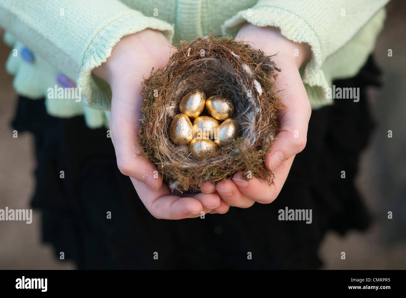 Girl holding golden eggs in a bird nest Stock Photo