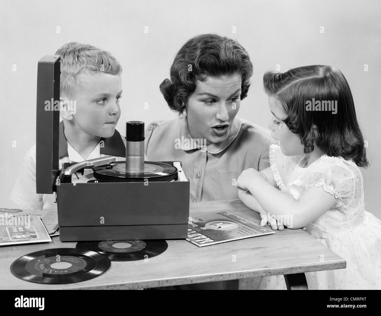 1950s MOTHER DAUGHTER & SON LISTENING TO 45'S ON PORTABLE RECORD PLAYER Stock Photo
