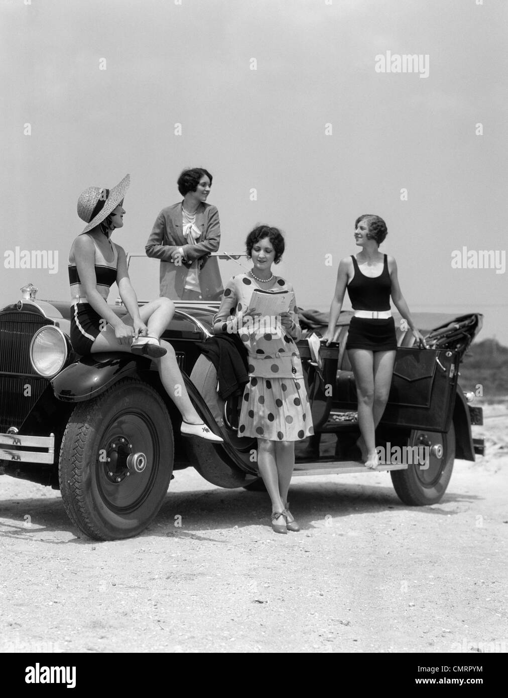 1920s 1930s FOUR WOMEN IN DRESSES AND BATHING SUITS GATHERED AROUND CONVERTIBLE TOURING CAR AT SEASHORE BEACH Stock Photo