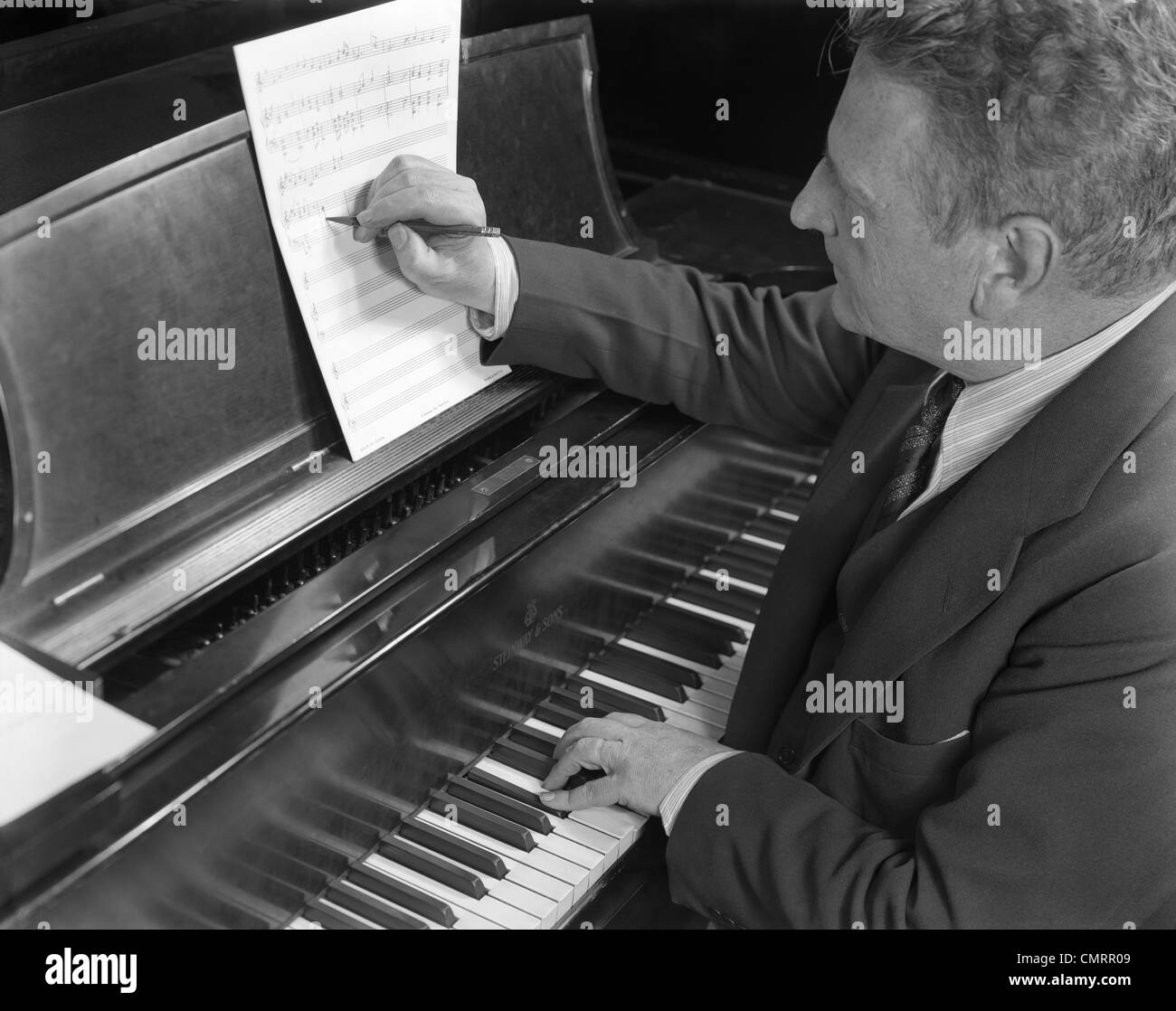 1930s 1940s MUSIC COMPOSER MAN SITTING AT PIANO KEYBOARD PLAYING AND WRITING DOWN MUSIC NOTES MUSICIAN Stock Photo