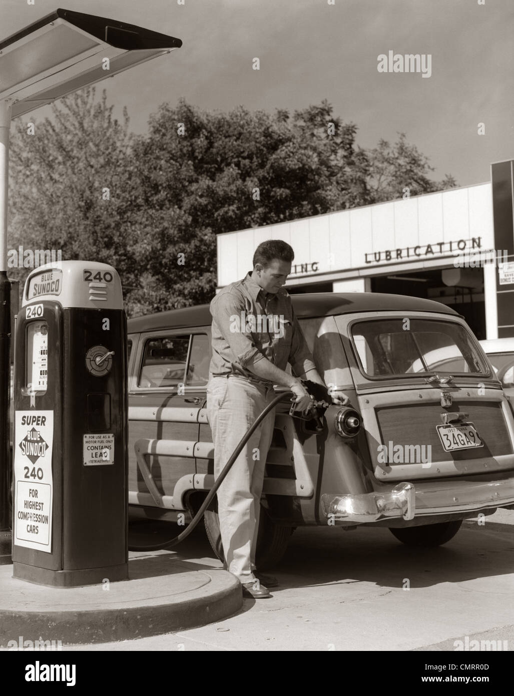 1950s SERVICE STATION ATTENDANT MAN FILLING GAS TANK OF WOOD BODY STATION WAGON Stock Photo