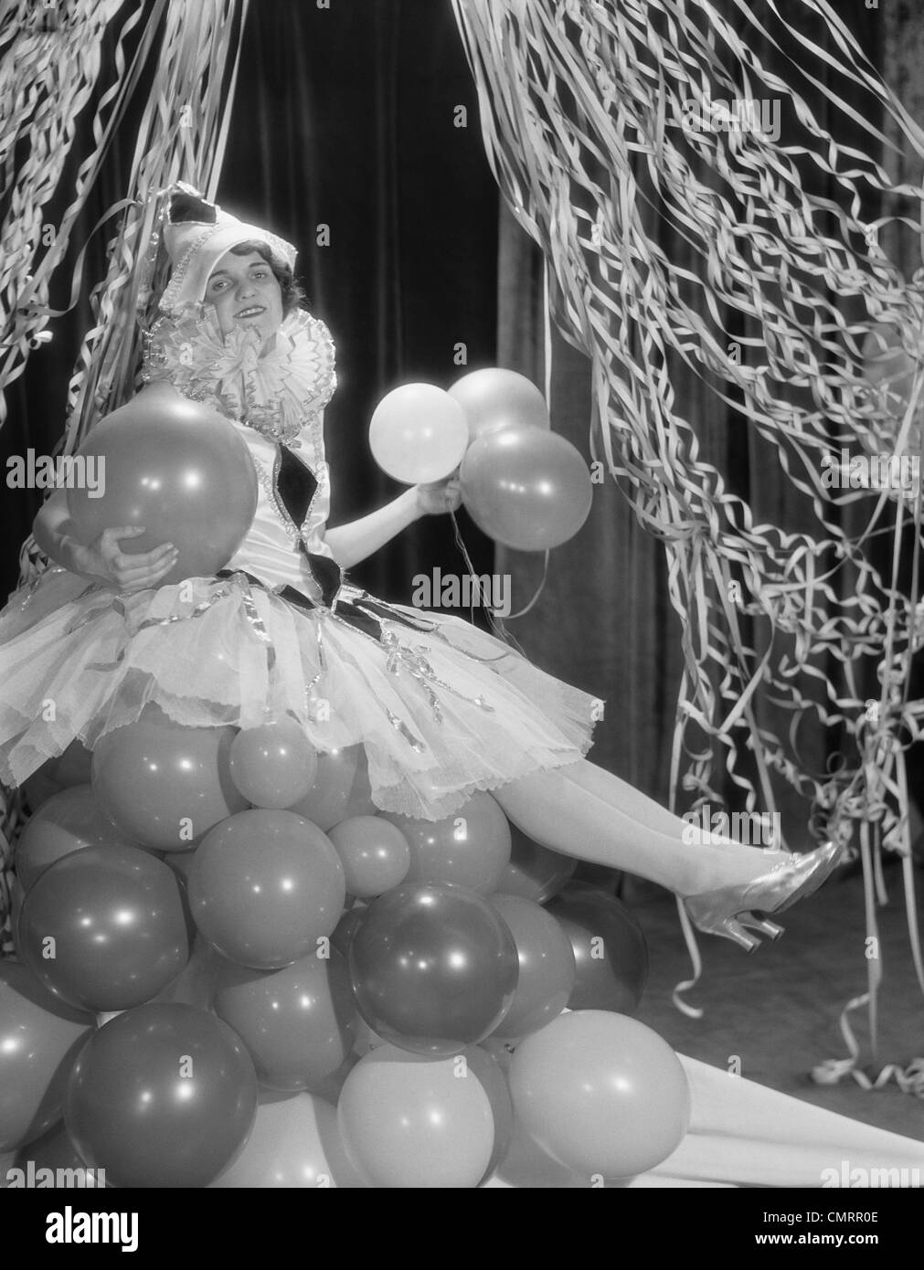 1920s WOMAN DRESSED IN HARLEQUIN COSTUME SITTING ON STACK OF BALLOONS Stock Photo