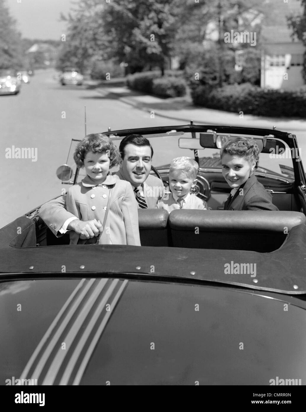1950s PORTRAIT WELL DRESSED FAMILY MOM DAD SON DAUGHTER IN CONVERTIBLE CAR TOP DOWN LOOKING AT CAMERA OVER BACK OF TRUNK Stock Photo