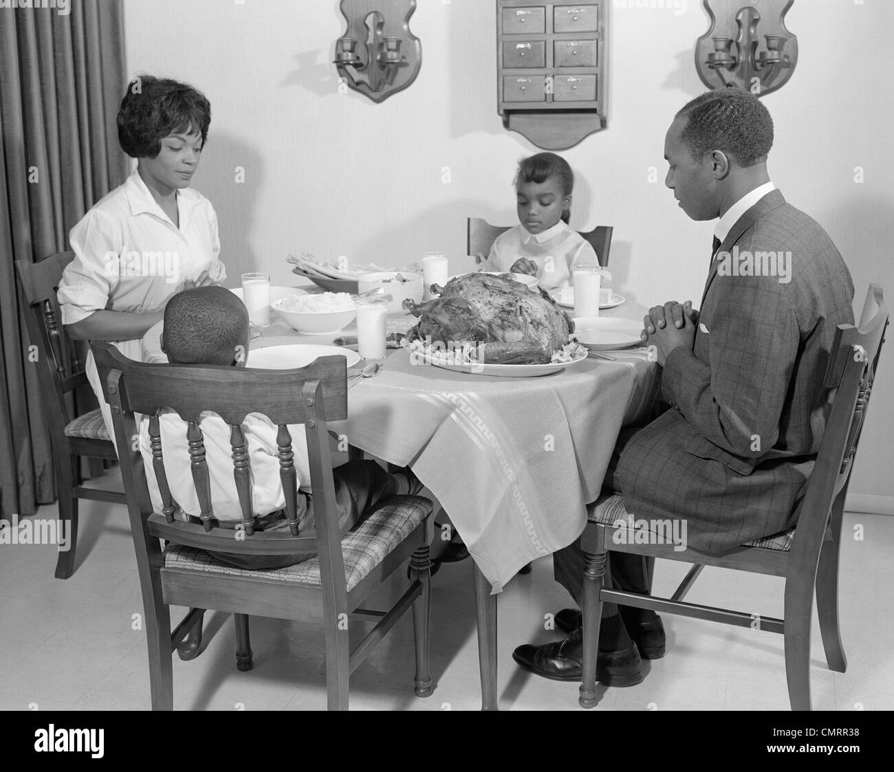 1960s AFRICAN-AMERICAN FAMILY AT DINING TABLE WITH TURKEY SAYING GRACE PRAYING Stock Photo