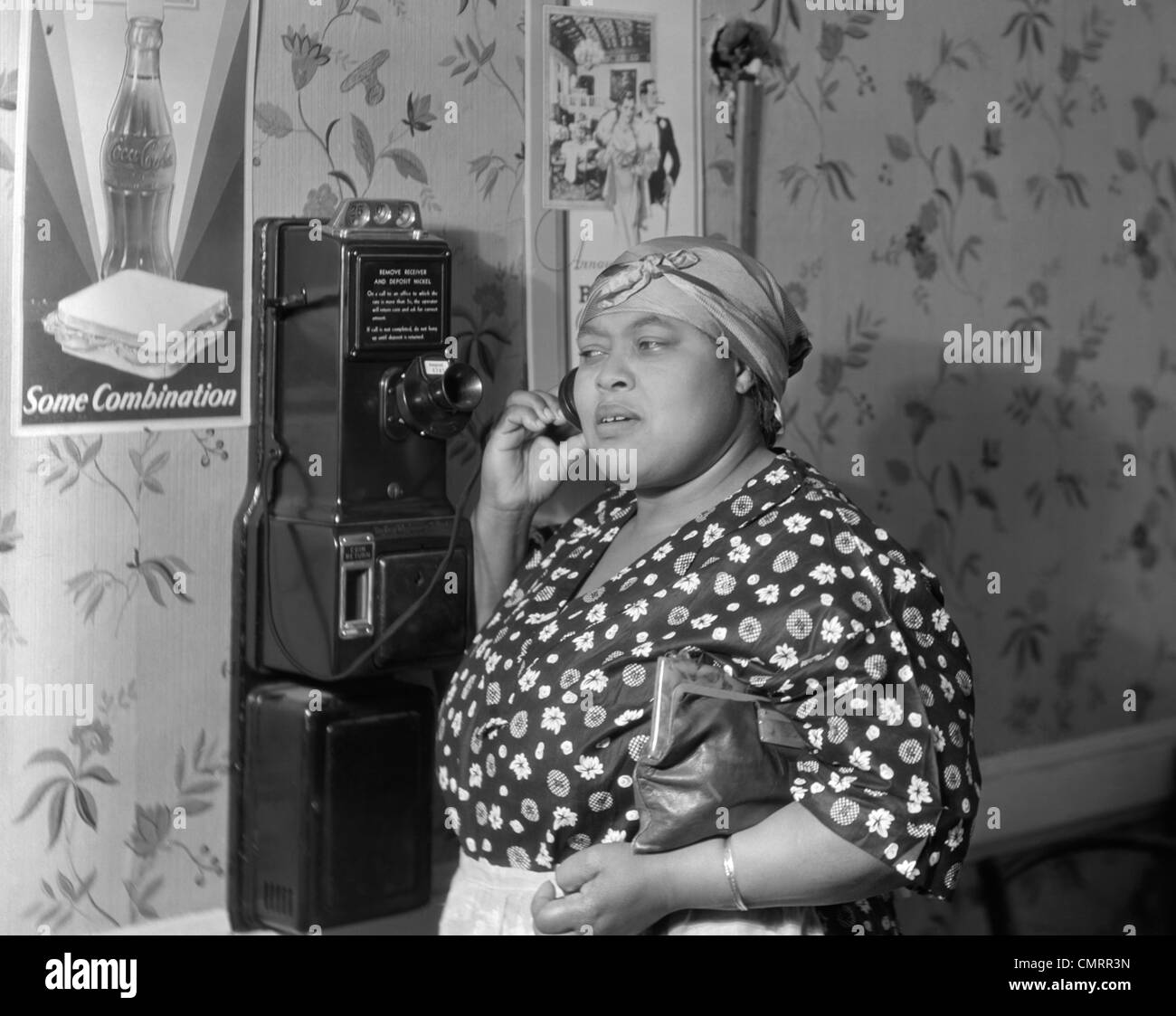 1930s 1940s AFRICAN AMERICAN WOMAN TALKING ON PUBLIC PAY WALL TELEPHONE IN PUBLIC RESTAURANT Stock Photo