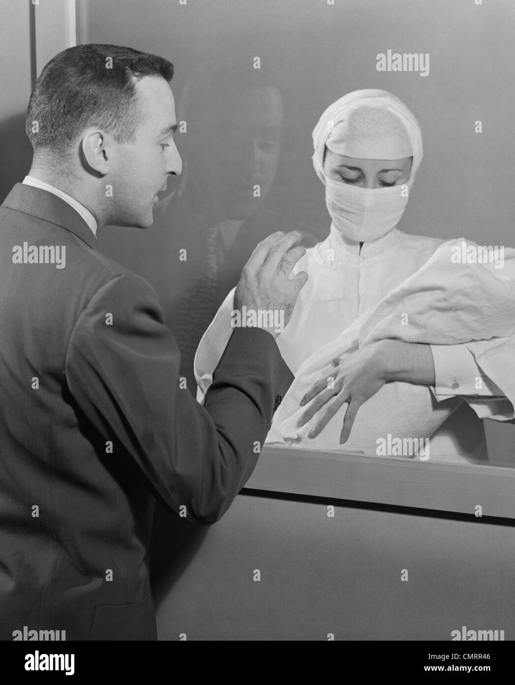 1950s FEMALE NURSE HOLDING INFANT UP TO FATHER AT NURSERY WINDOW Stock Photo