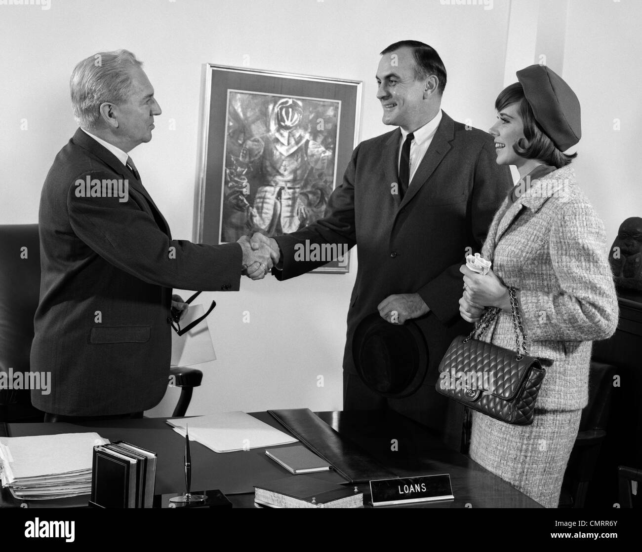 1960s COUPLE HUSBAND AND WIFE SHAKING HANDS WITH BANK LOAN MANAGER BUSINESS INDOOR Stock Photo