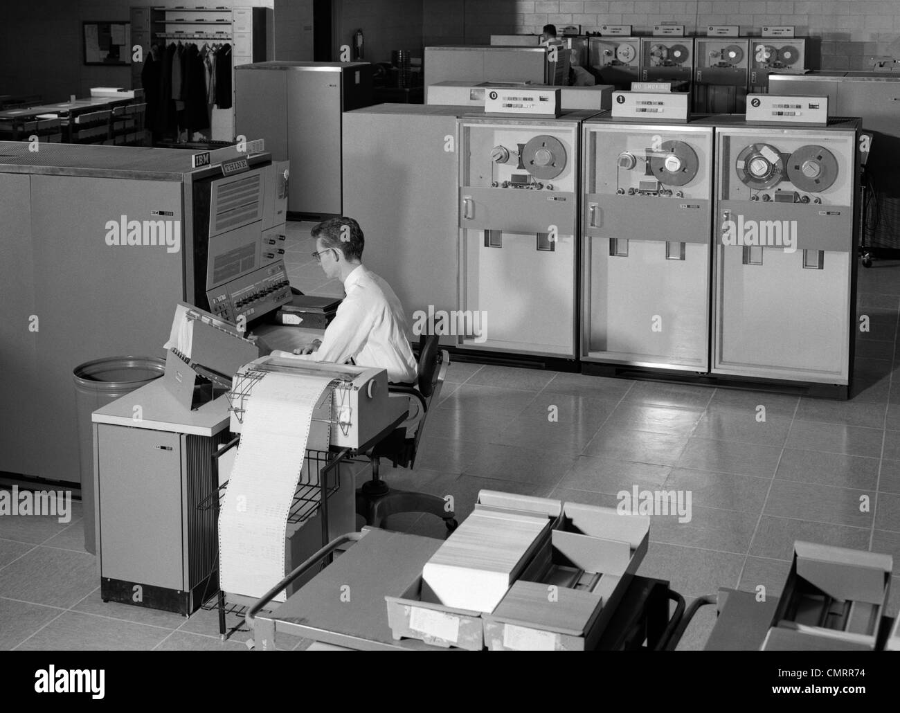 1960s-man-programming-large-mainframe-computer-surrounded-by-data-tape-drives-indoor-stock-photo