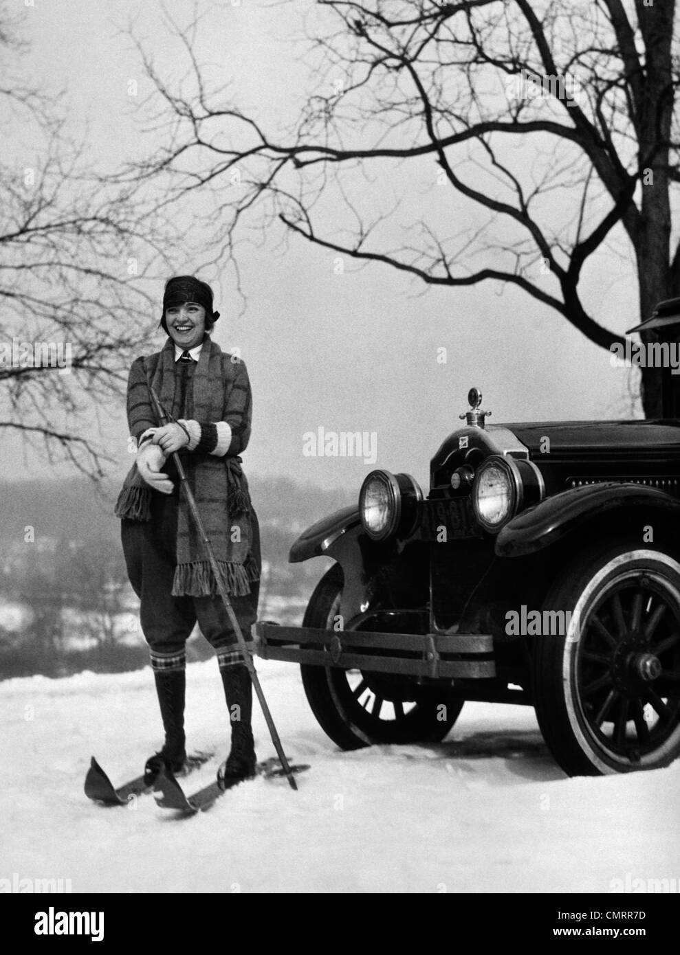 1920s WOMAN ON SKIS STANDING IN FRONT OF CAR PULLING ON GLOVE Stock Photo