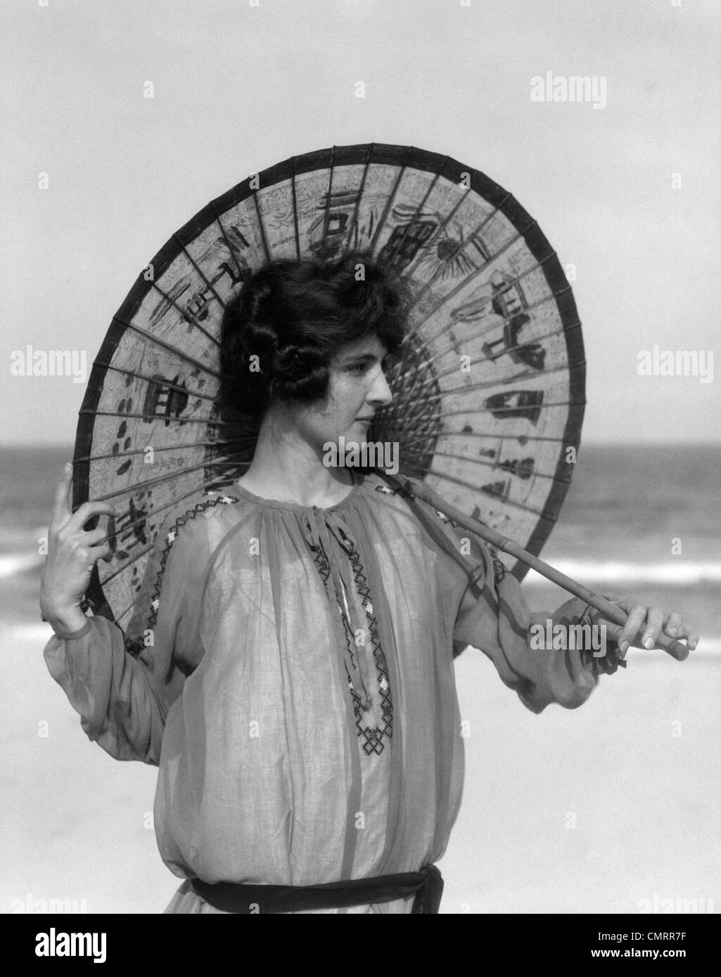 1920s WOMAN STANDING ON BEACH HOLDING ORIENTAL UMBRELLA LOOKING OFF TO SIDE Stock Photo