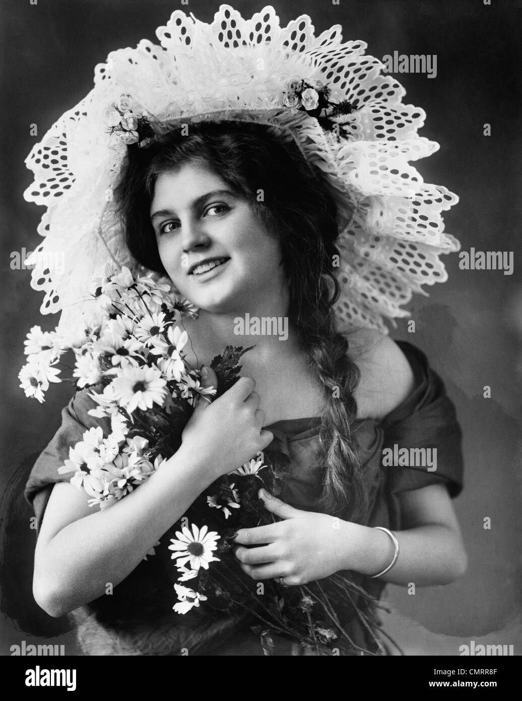 1900s 1910s TURN OF THE CENTURY WOMAN WITH LONG BRAIDS WEARING FANCY LACE HAT & HOLDING BOUQUET OF BLACK-EYED SUSAN FLOWERS Stock Photo
