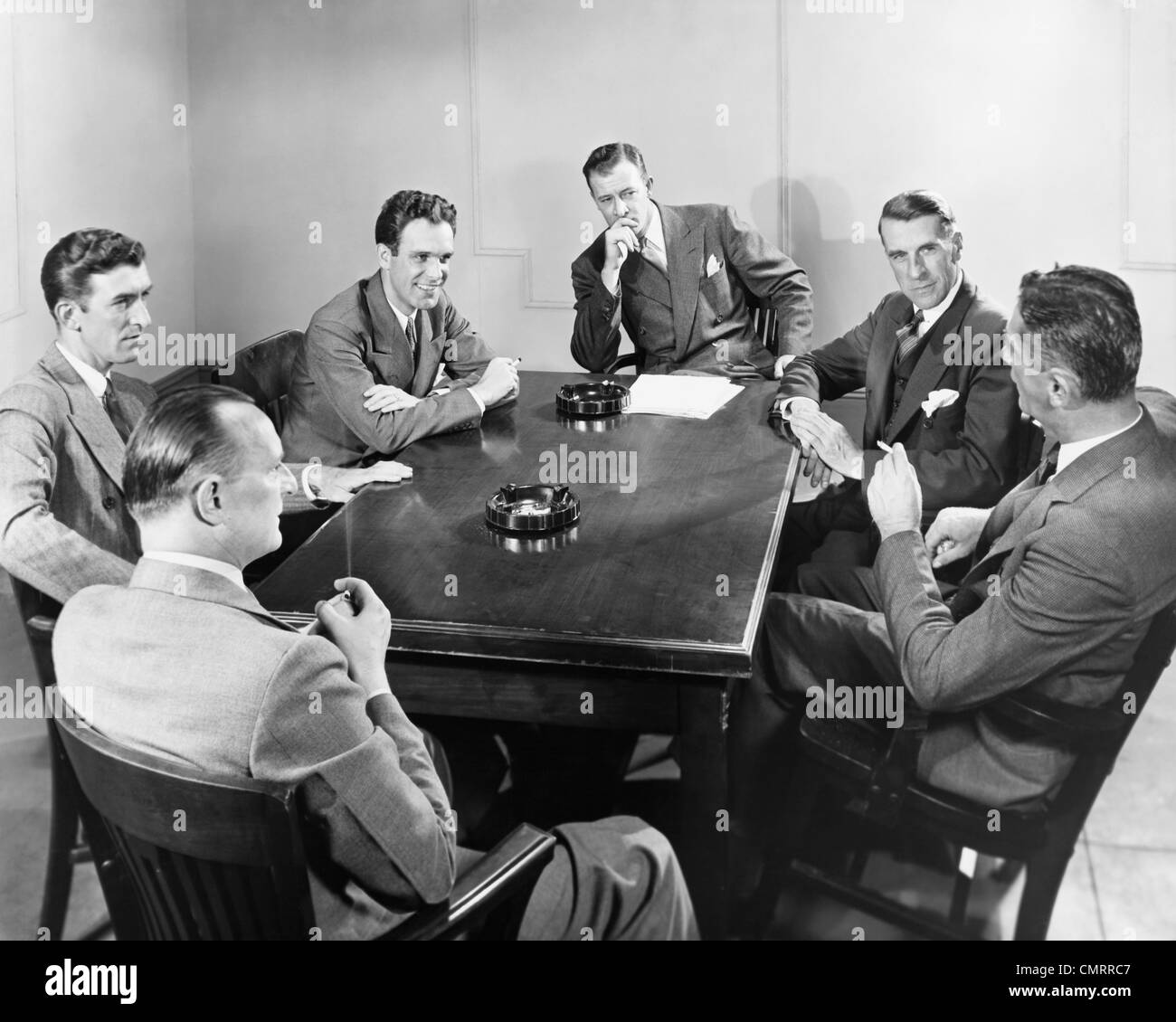 1930s 1940s 6 BUSINESSMEN MEETING IN BOARDROOM AROUND TABLE WITH ASHTRAYS Stock Photo