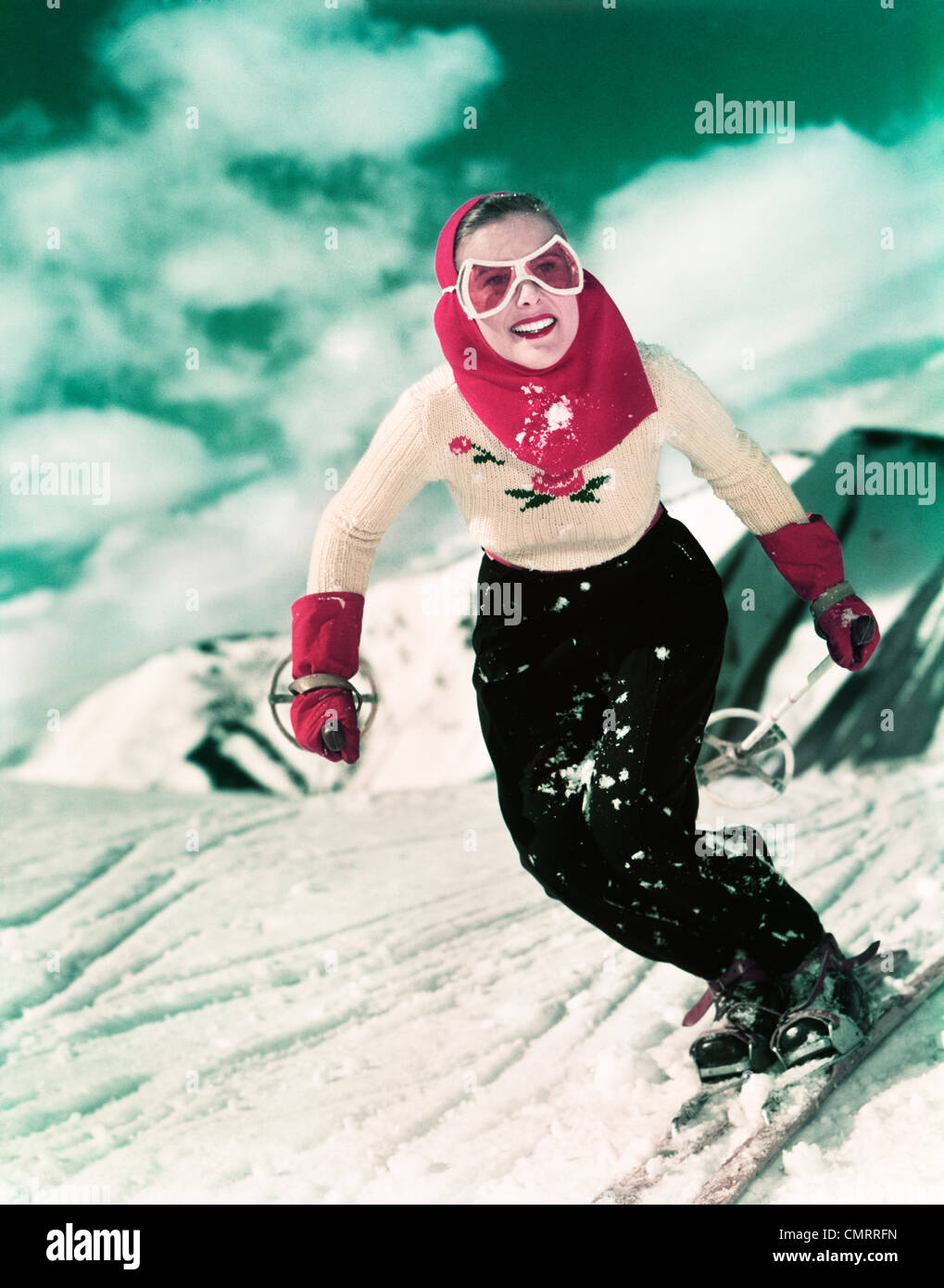 1940s 1950s SMILING WOMAN SKIING DOWNHILL WEARING GOGGLES RED HOOD AND RED GLOVES Stock Photo