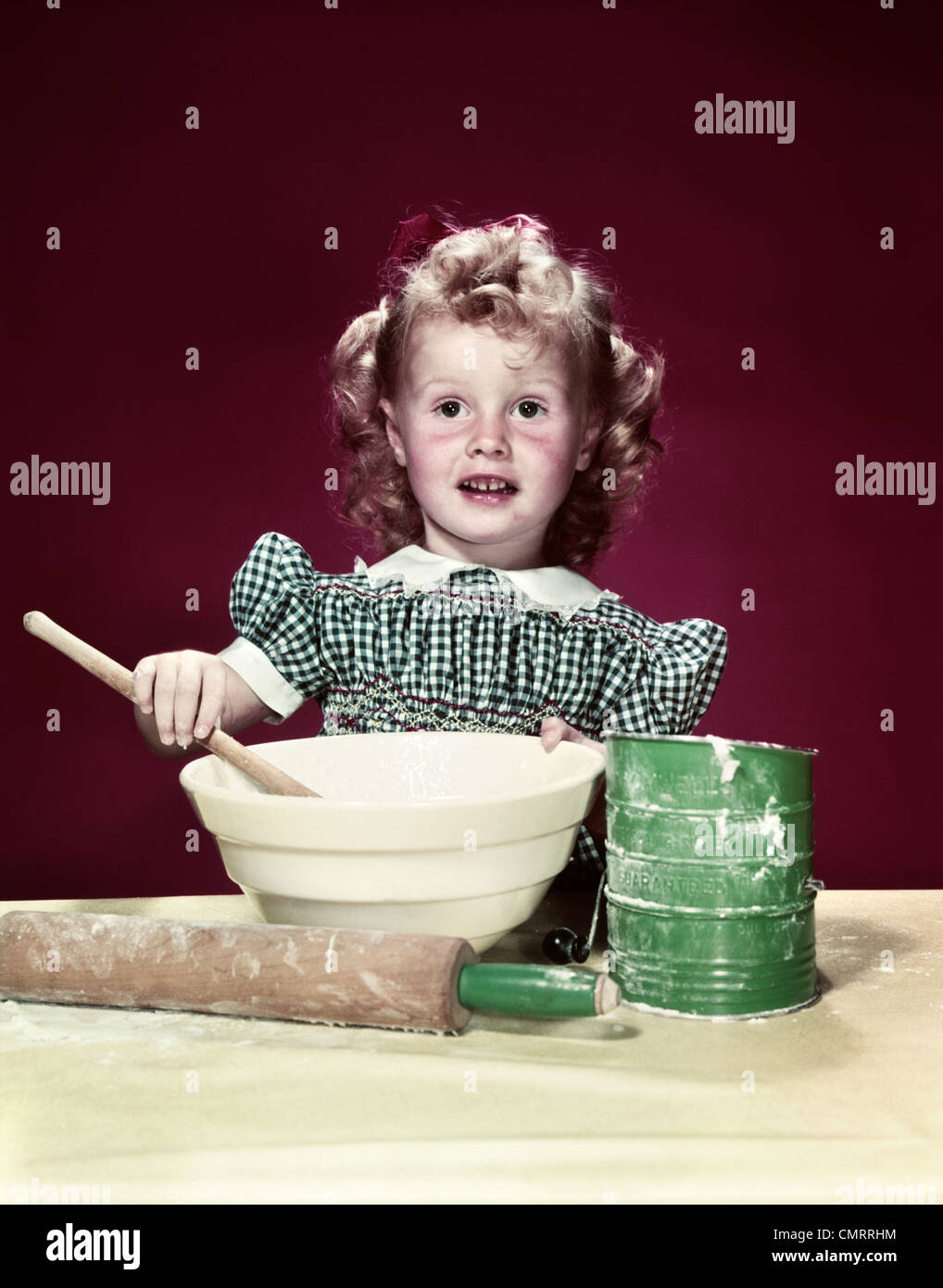 1940s GIRL WEARING CHECKED DRESS MIXING INGREDIENTS IN BOWL WITH WOODEN SPOON Stock Photo