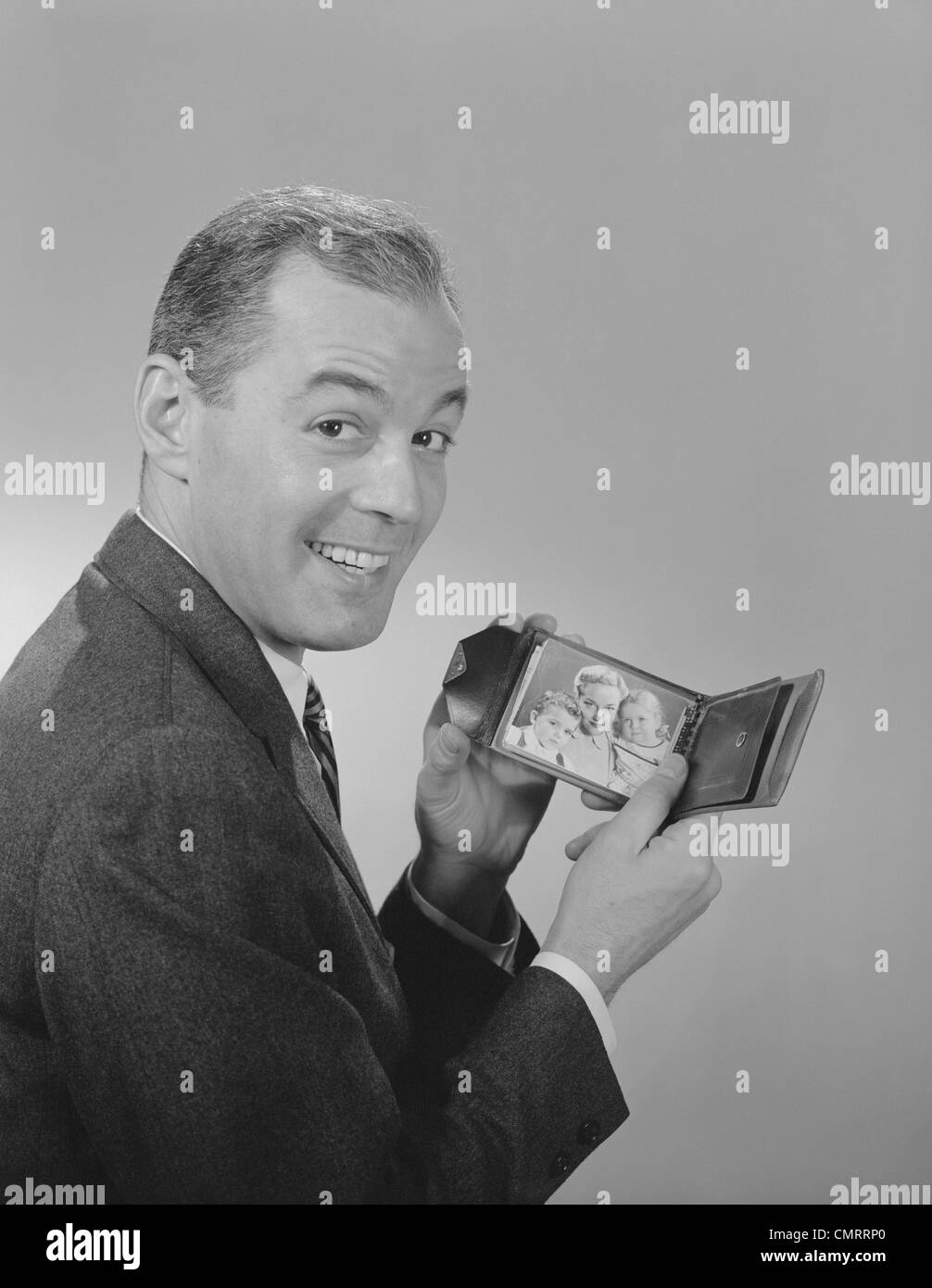 1950s 1960s MAN SMILING HOLDING  WALLET SHOWING PHOTO OF FAMILY LOOKING AT CAMERA Stock Photo