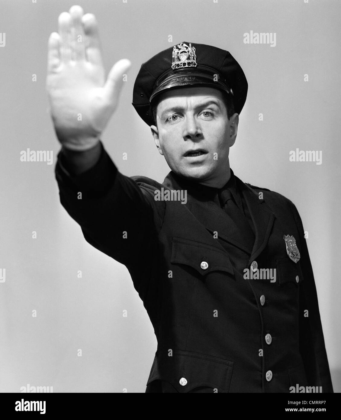 1950s MAN POLICEMAN IN UNIFORM HOLDING HAND UP IN AIR TOWARDS CAMERA STOP HALT WARNING LOOKING AT CAMERA Stock Photo