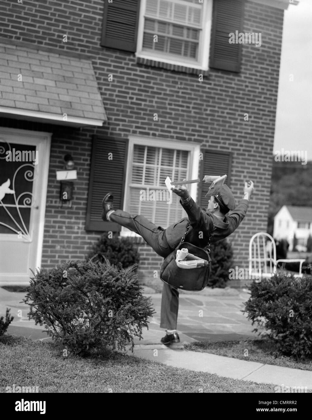 1950s MAN MAILMAN TRIPPING FALLING IN FRONT OF A SUBURBAN BRICK HOUSE ACCIDENT Stock Photo