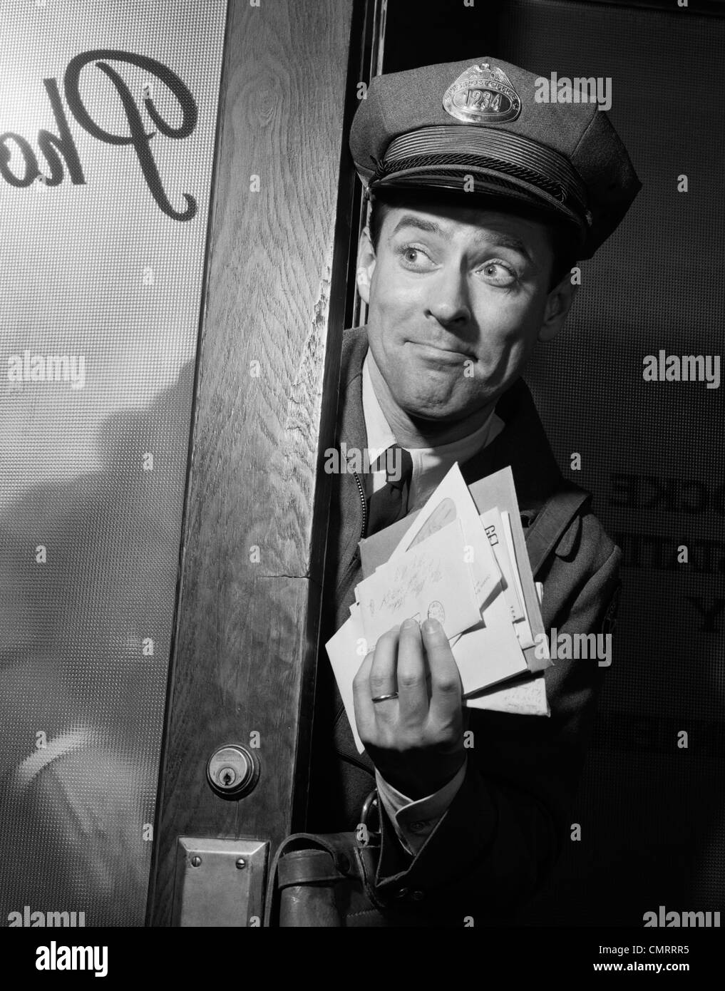 1960s MAN MAILMAN WITH HANDFUL OF LETTER MAIL COMING THROUGH DOOR Stock Photo