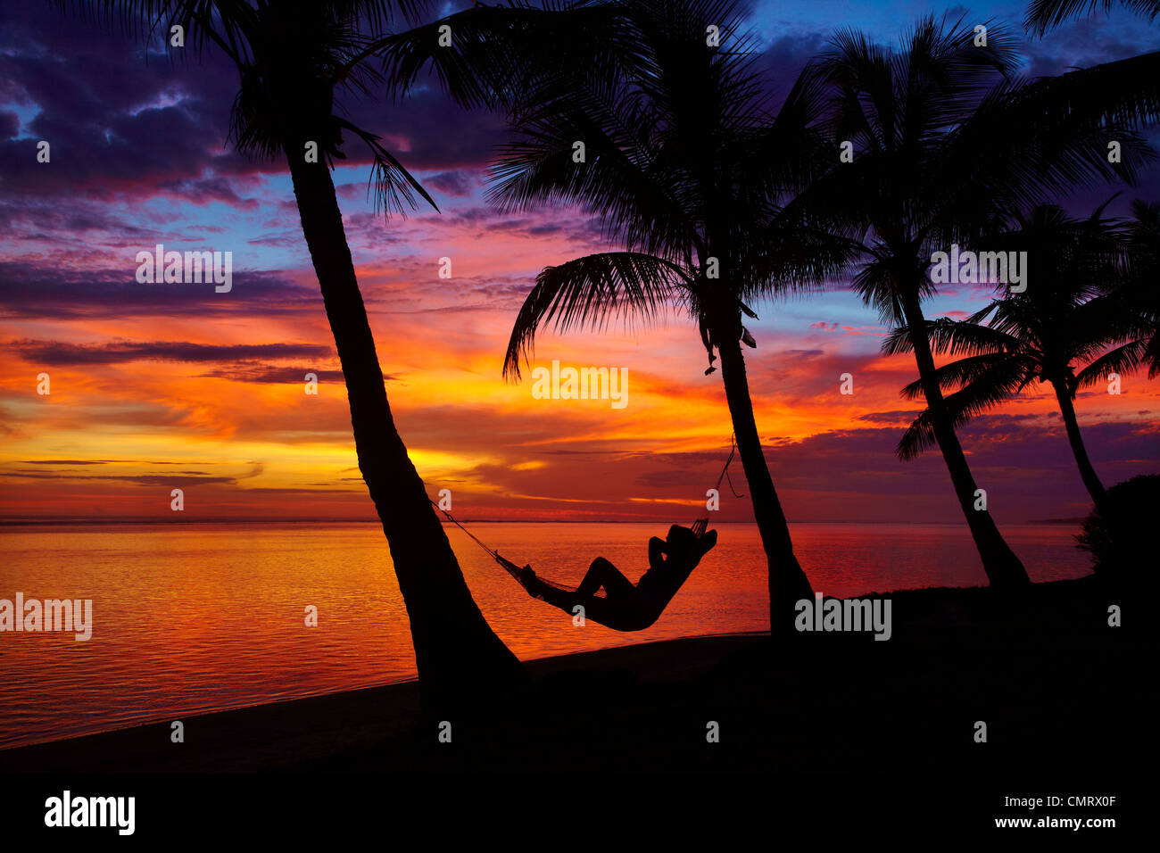 Woman in hammock, and palm trees at sunset, Coral Coast, Viti Levu, Fiji, South Pacific Stock Photo