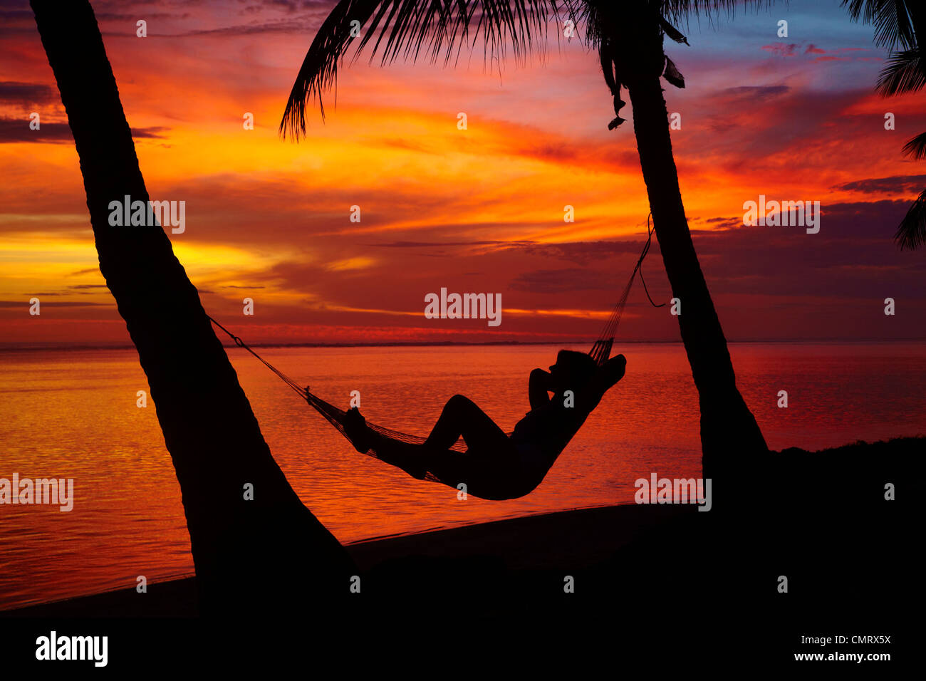 Woman in hammock, and palm trees at sunset, Coral Coast, Viti Levu, Fiji, South Pacific Stock Photo